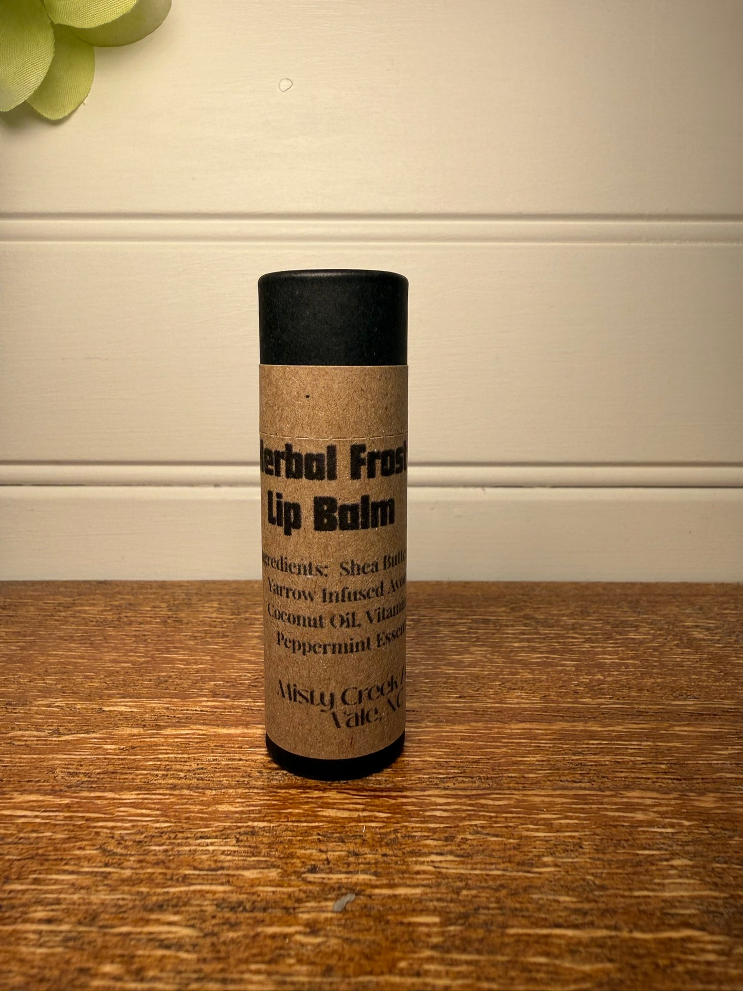 Lip balm container with black lid and cork-like body on a wooden surface.
