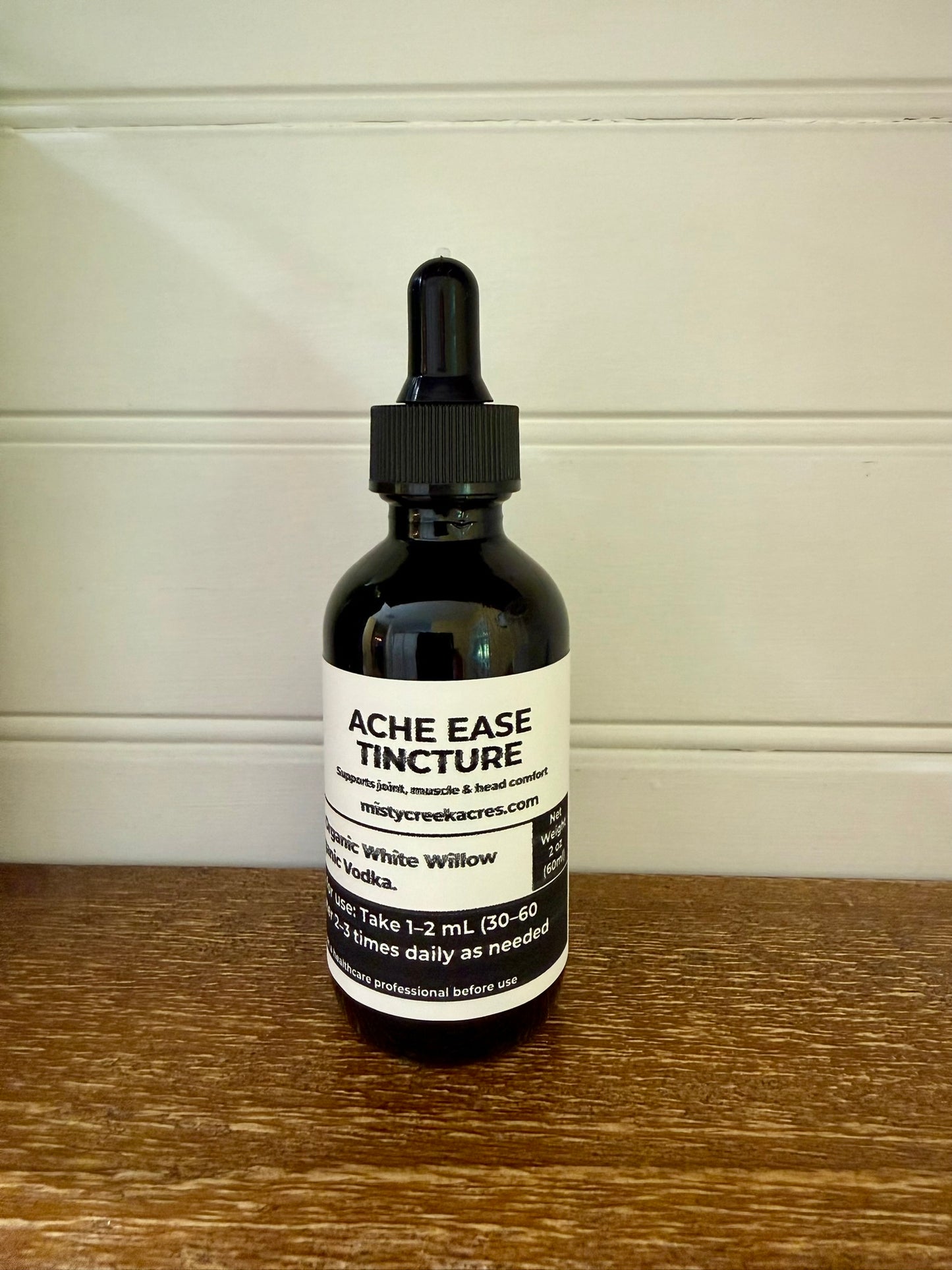 Bottle of Ache Ease Tincture on a wooden surface with a white background