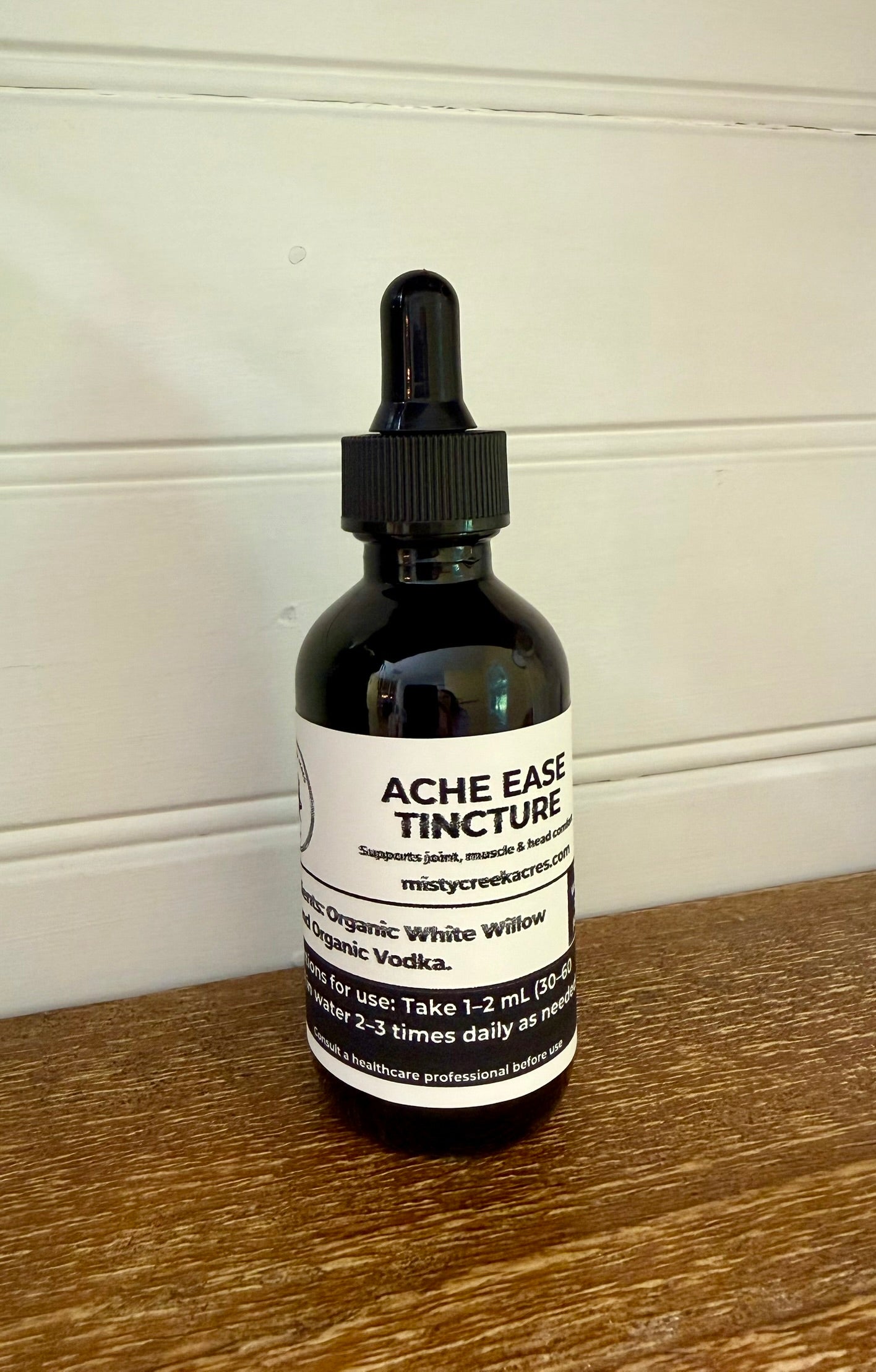 Bottle of Acme Ease Tincture on a wooden surface with a white wall background