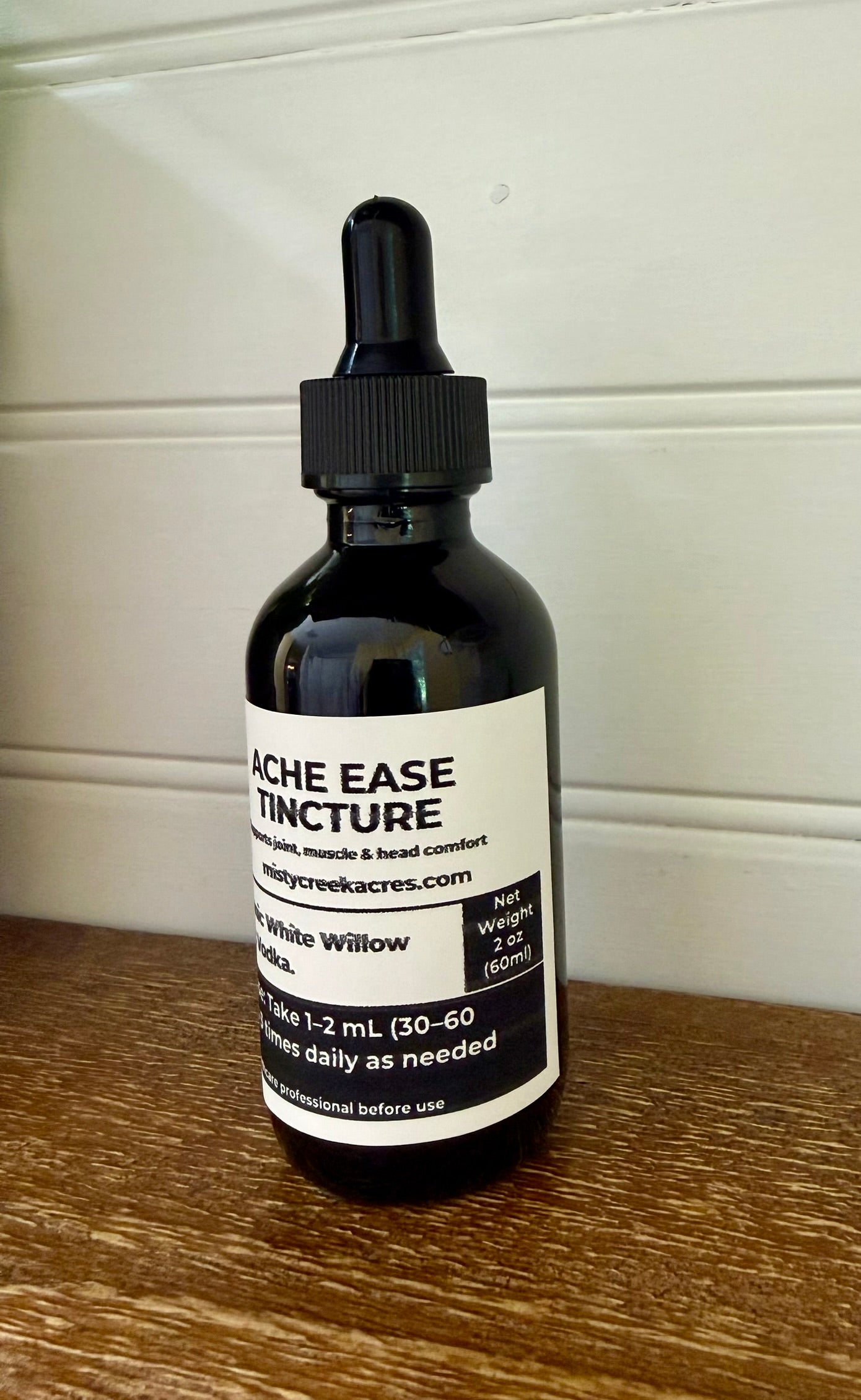 Bottle of Ache Ease Tincture on a wooden surface with a white background