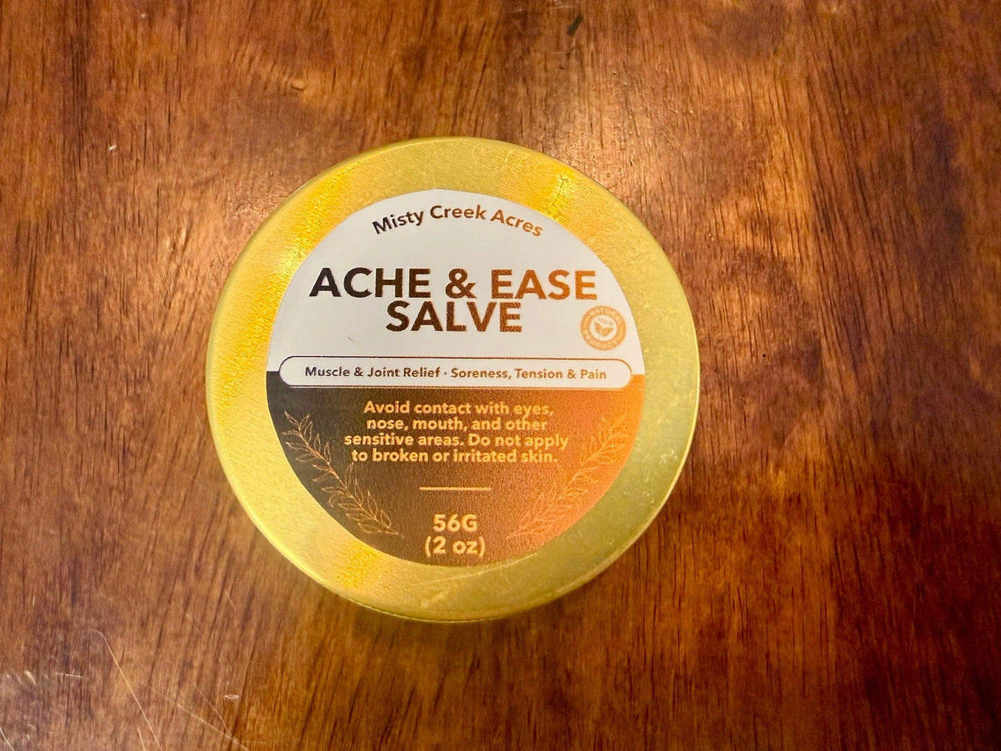 Jar of Ache & Ease Salve on a wooden surface