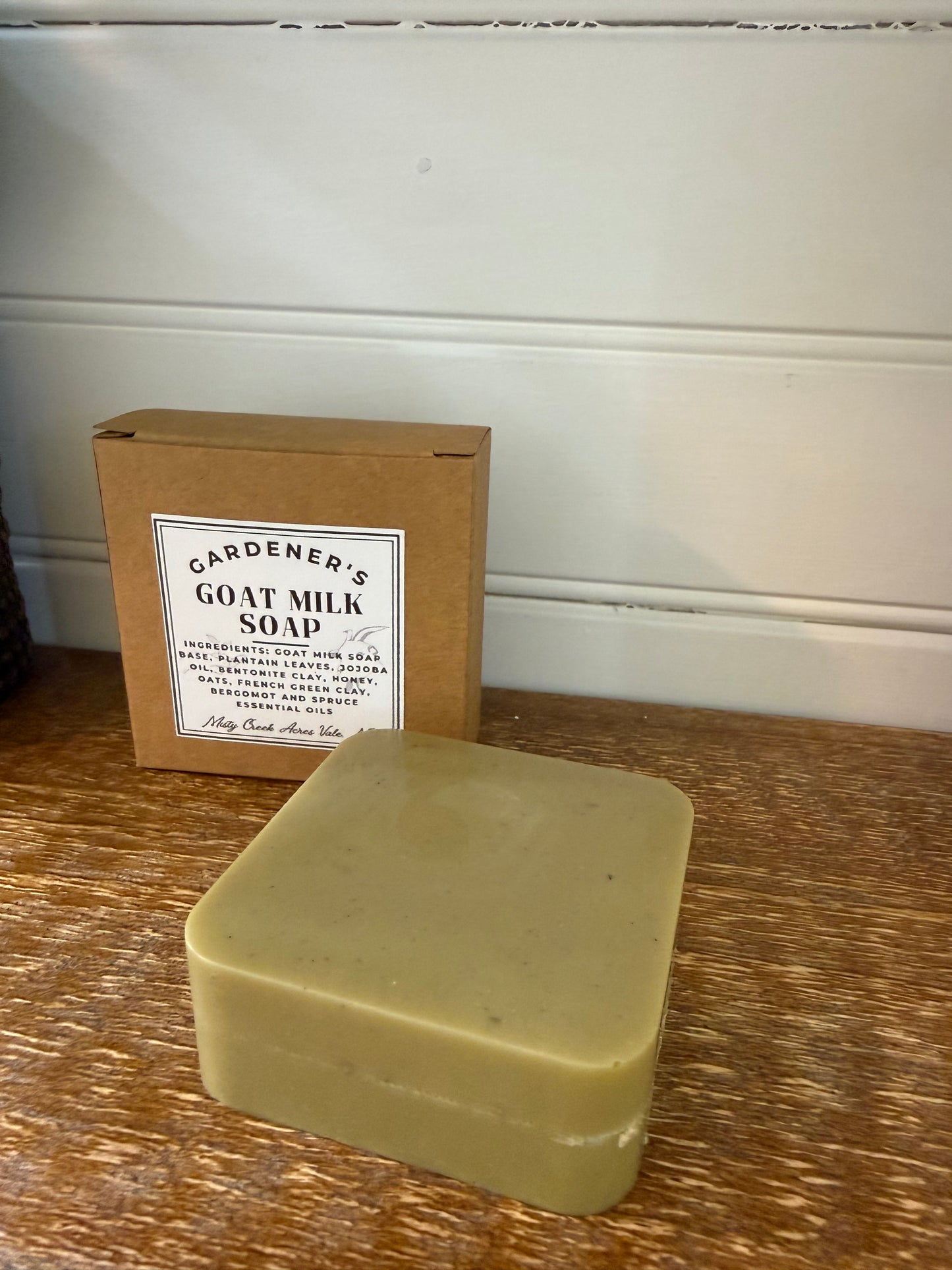 Bar of soap on a wooden surface next to a cardboard box labeled 'Gardener's Goat Milk Soap'.