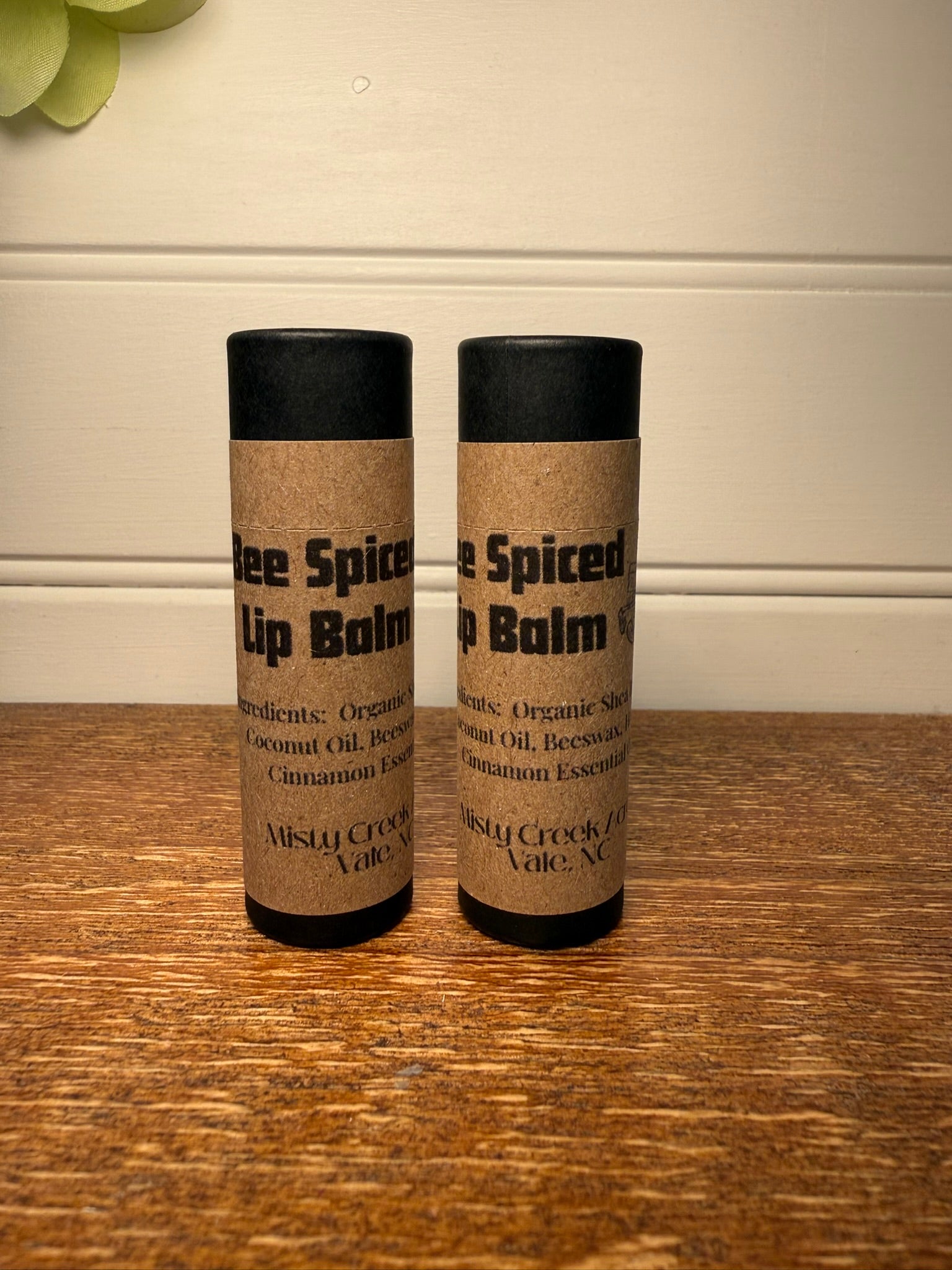 Two lip balm containers with black lids on a wooden surface.