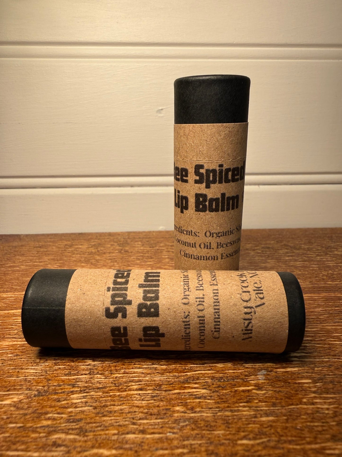 Two lip balm tubes with a cardboard label on a wooden surface.