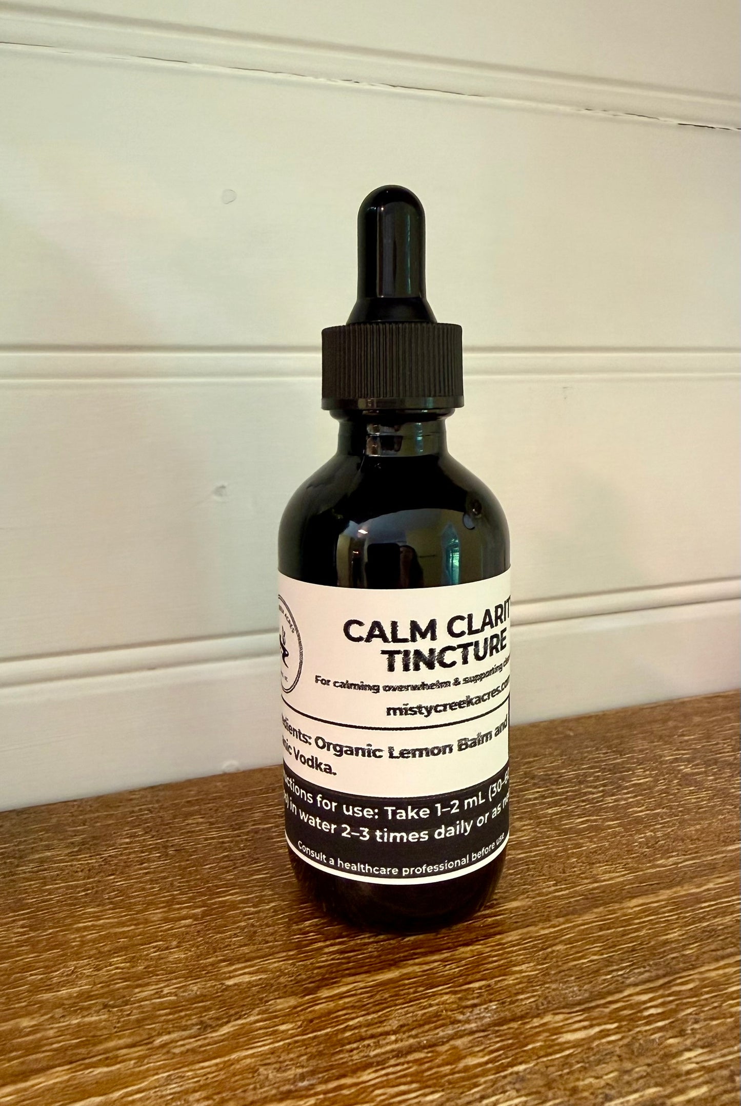 Bottle of Calm Clear Tincture on a wooden surface with a white wall background