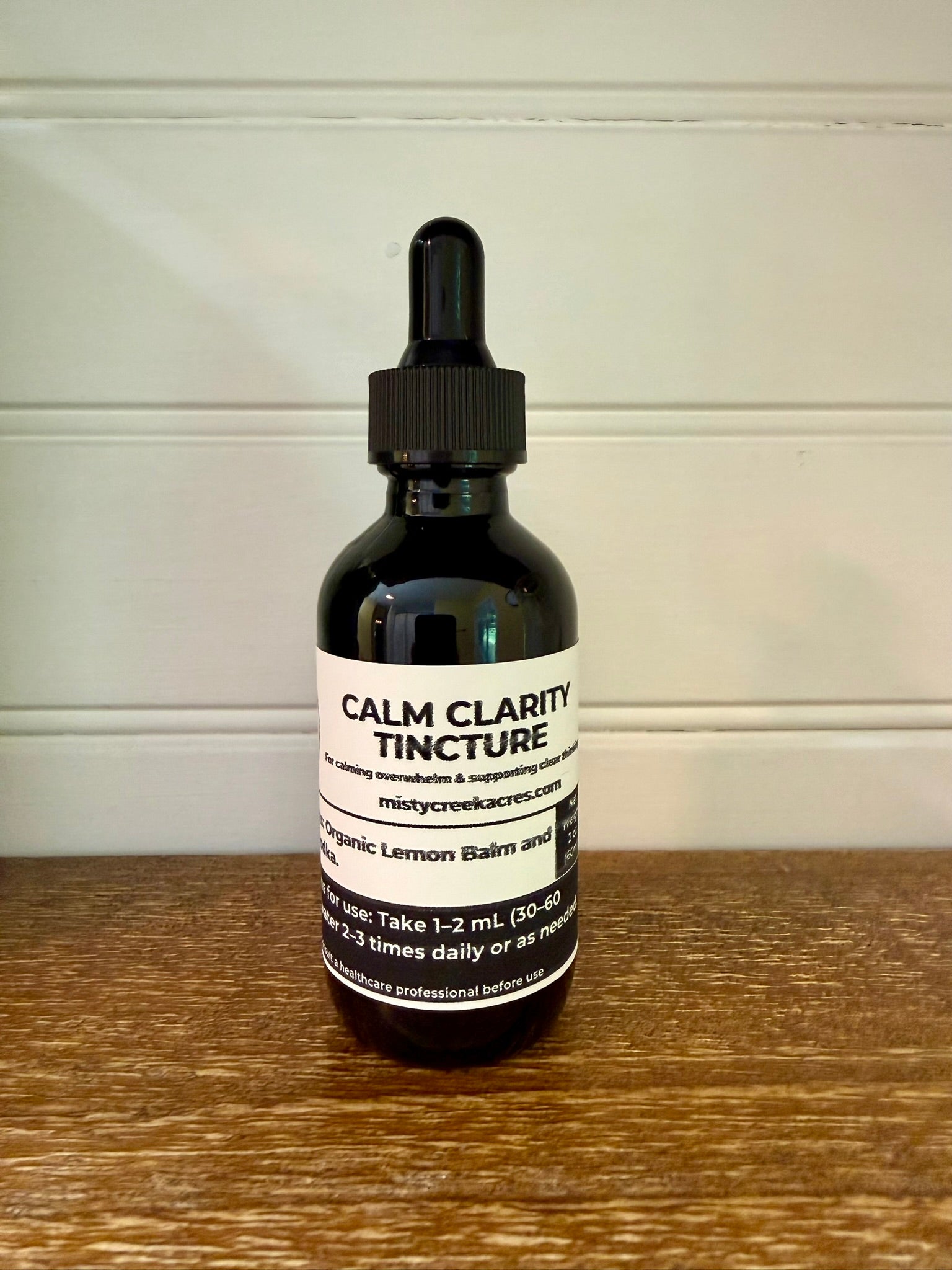 Bottle of Calm Clarity Tincture on a wooden surface with a white wall background