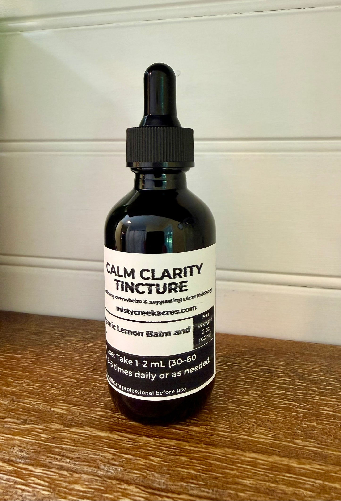 Bottle of Calm Clarity Tincture on a wooden surface with a white wall background