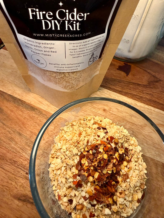 Glass bowl with a mixture of ingredients next to a Fire Cider DIY Kit on a wooden surface