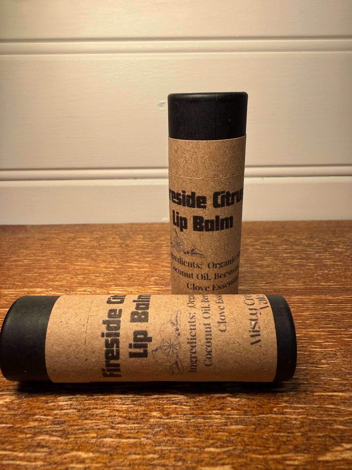 Two lip balm tubes with kraft paper wrapping on a wooden surface.