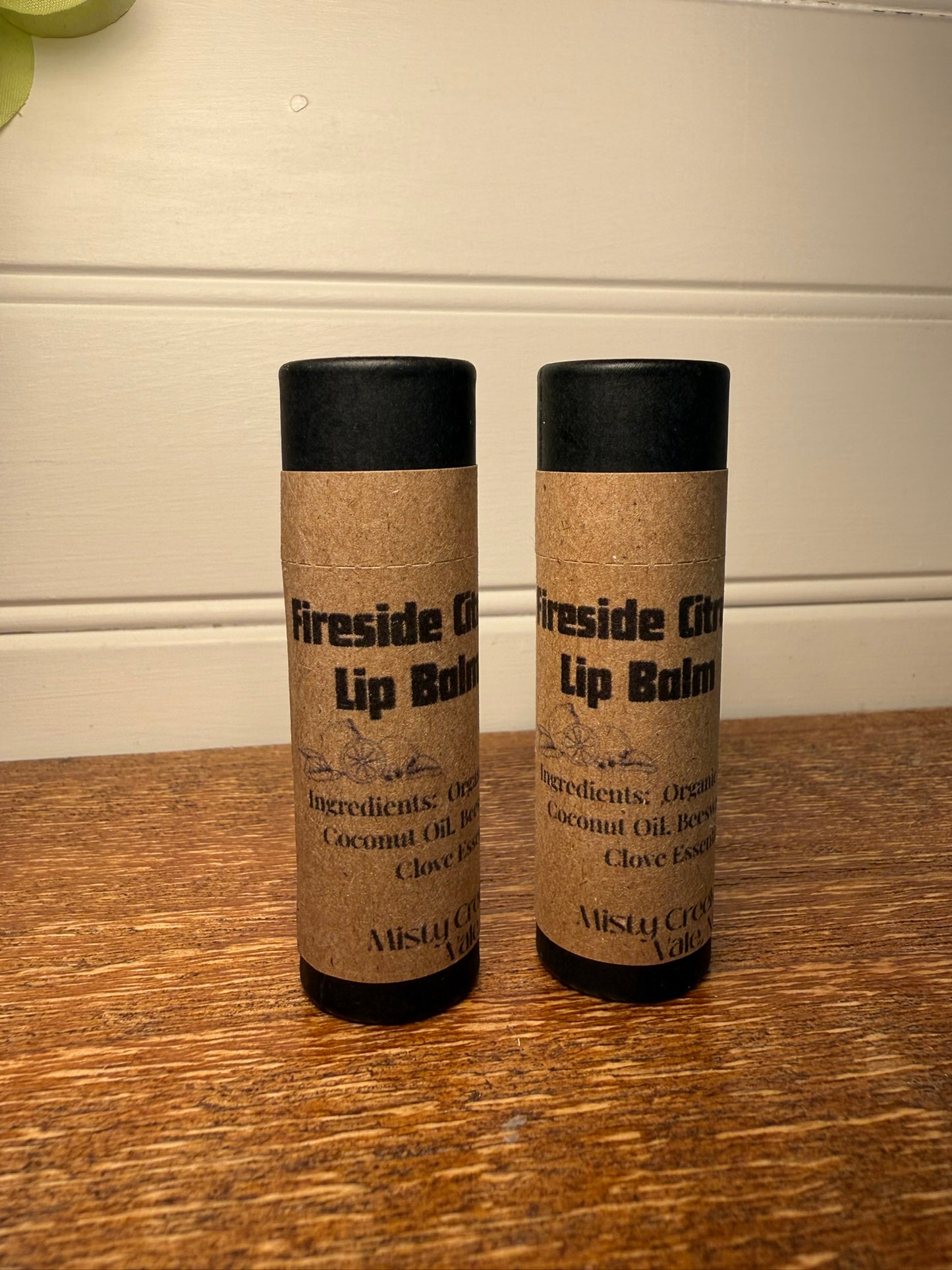 Two lip balm containers labeled 'Fireside Oils' on a wooden surface.