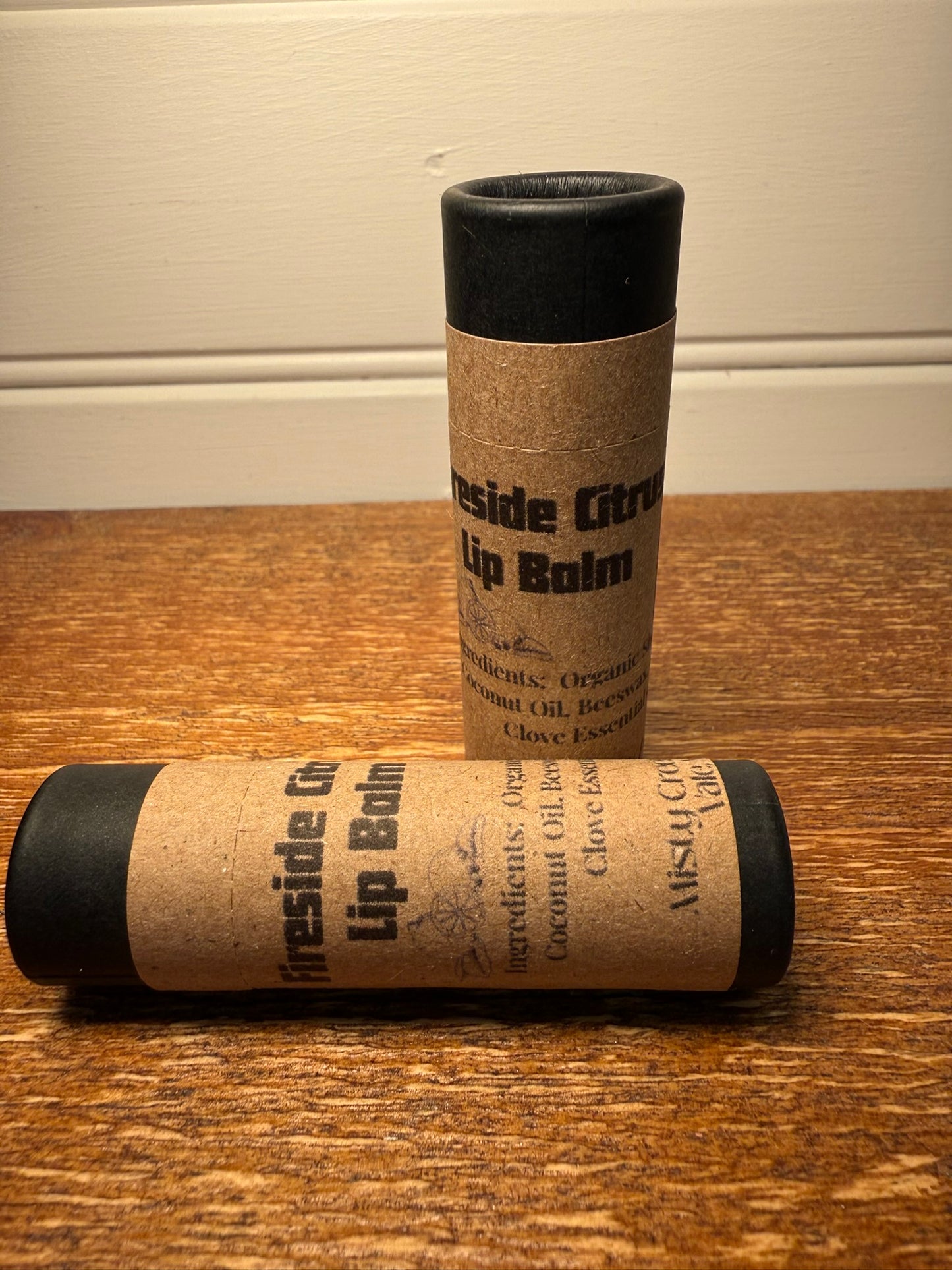 Two lip balm tubes with kraft paper wrapping on a wooden surface.