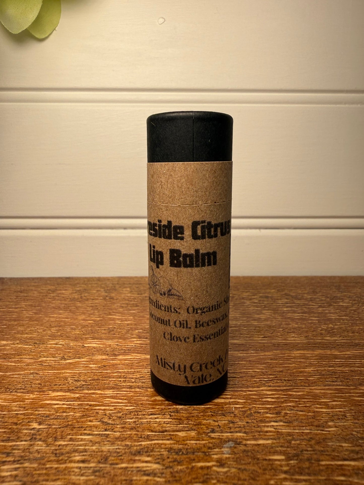 Lip balm container with kraft paper wrap and black lid on a wooden surface.