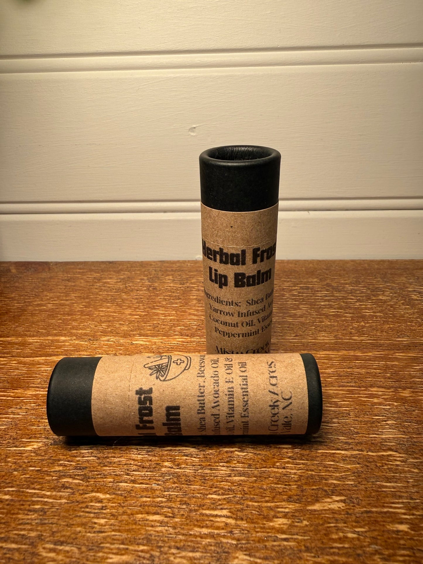 Two cylindrical lip balm containers on a wooden surface with a neutral background