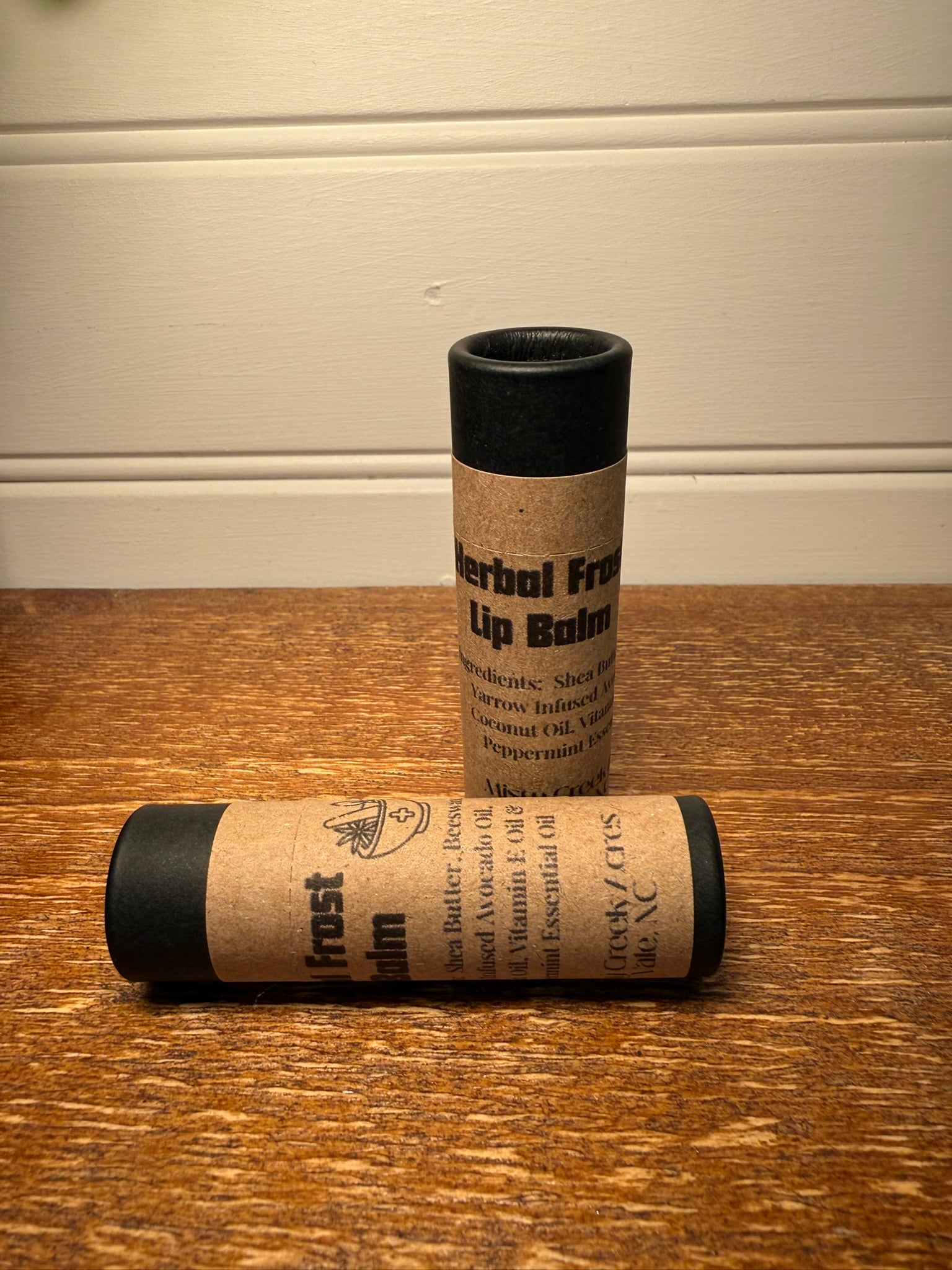 Two cylindrical lip balm containers on a wooden surface with a neutral background