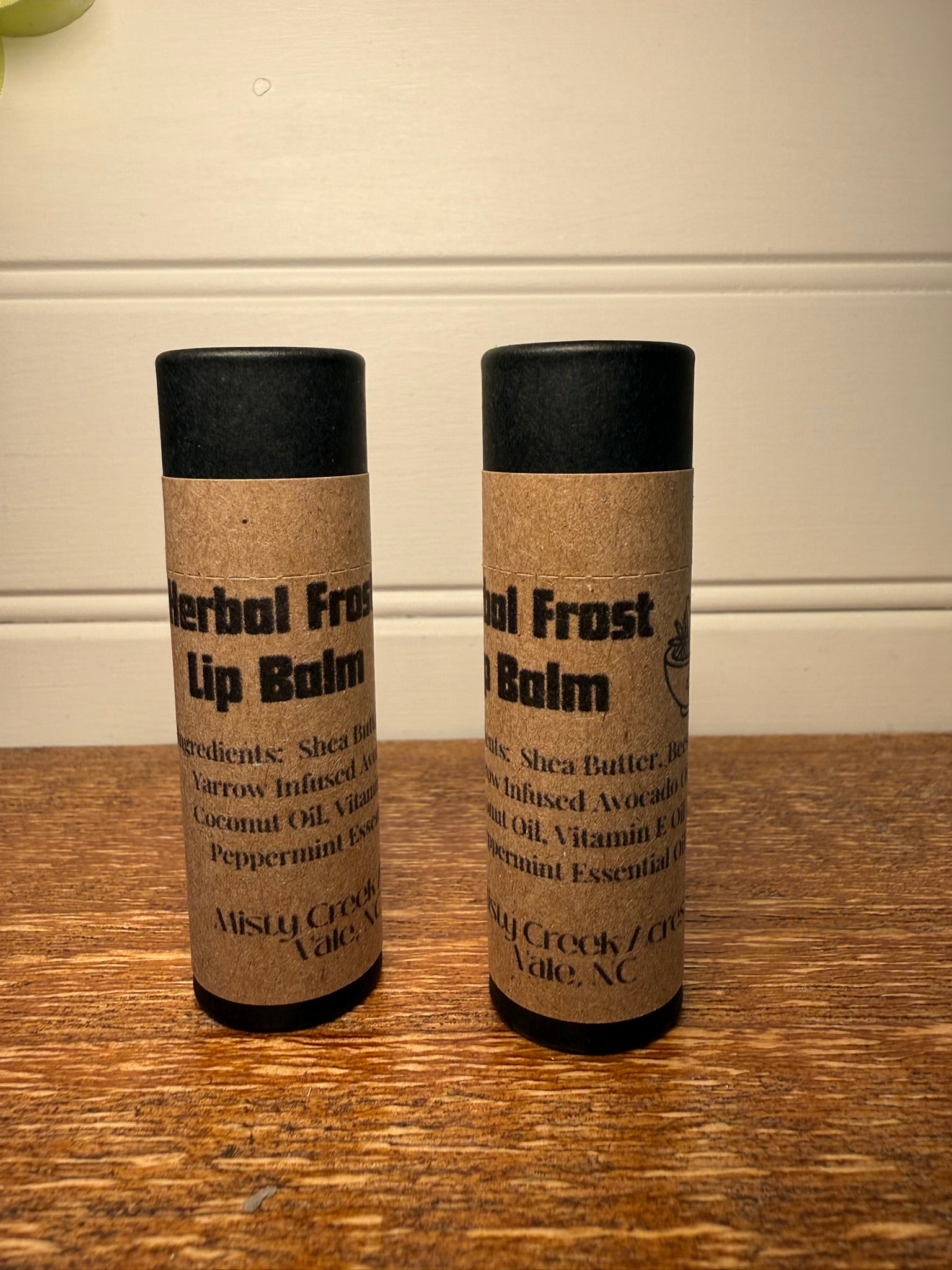 Two lip balm containers on a wooden surface with a neutral background