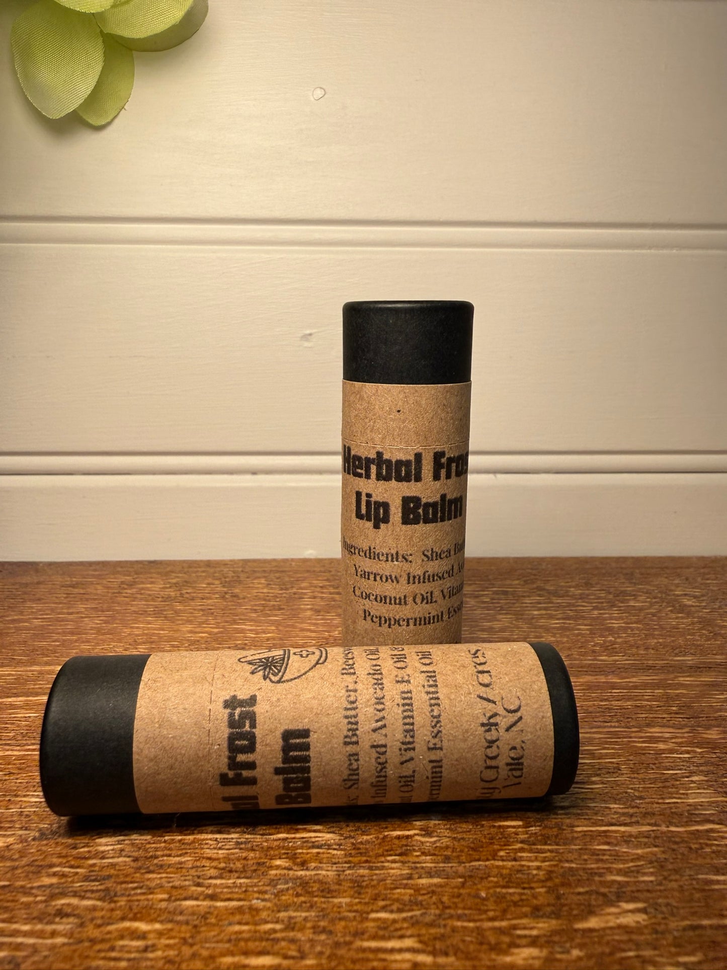 Two lip balm tubes with kraft paper wrapping on a wooden surface.