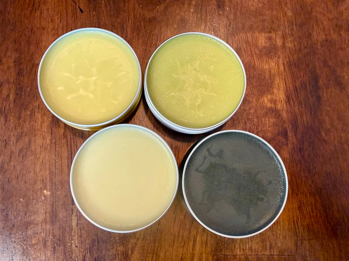 Four metal tins with greenish contents on a wooden surface