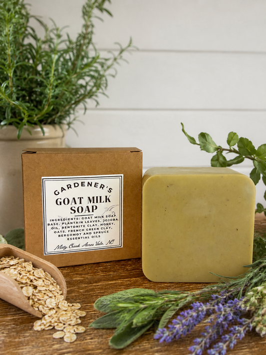 Bar of goat milk soap with packaging on a wooden surface with plants and oats.