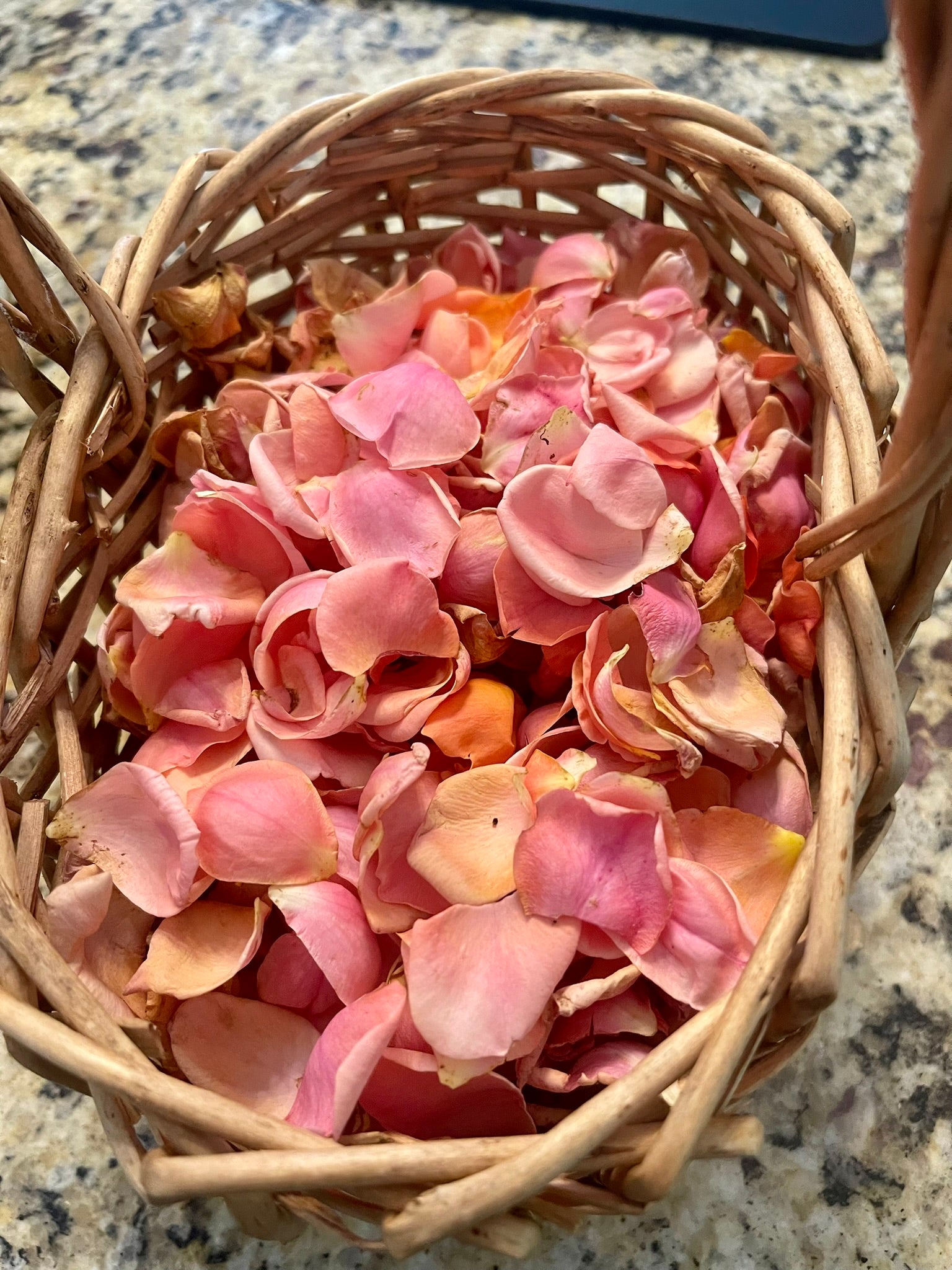 Basket filled with pink and orange flower petals on a marble surface