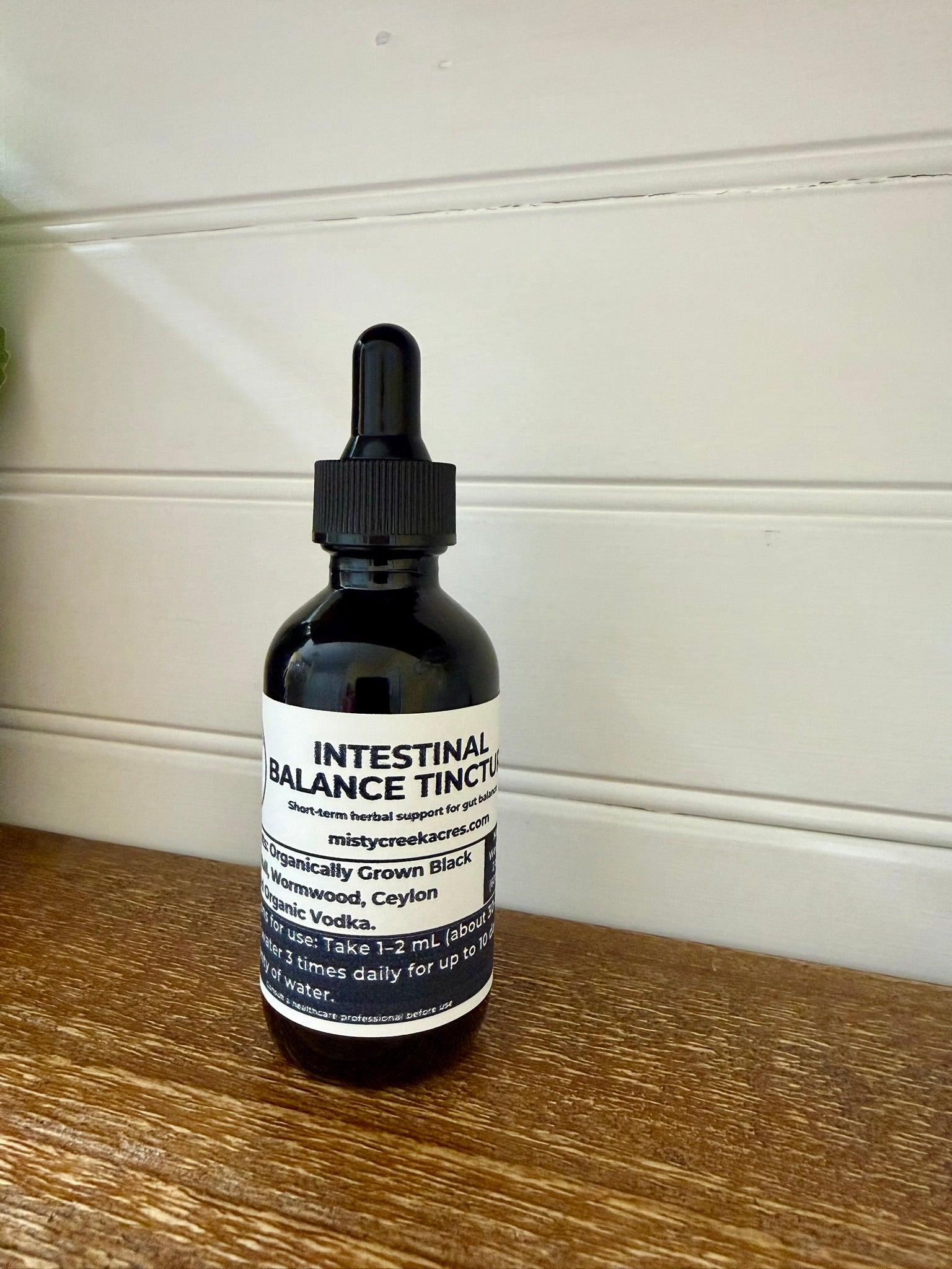Intestinal Balance Tincture bottle on a wooden surface with a white wall background