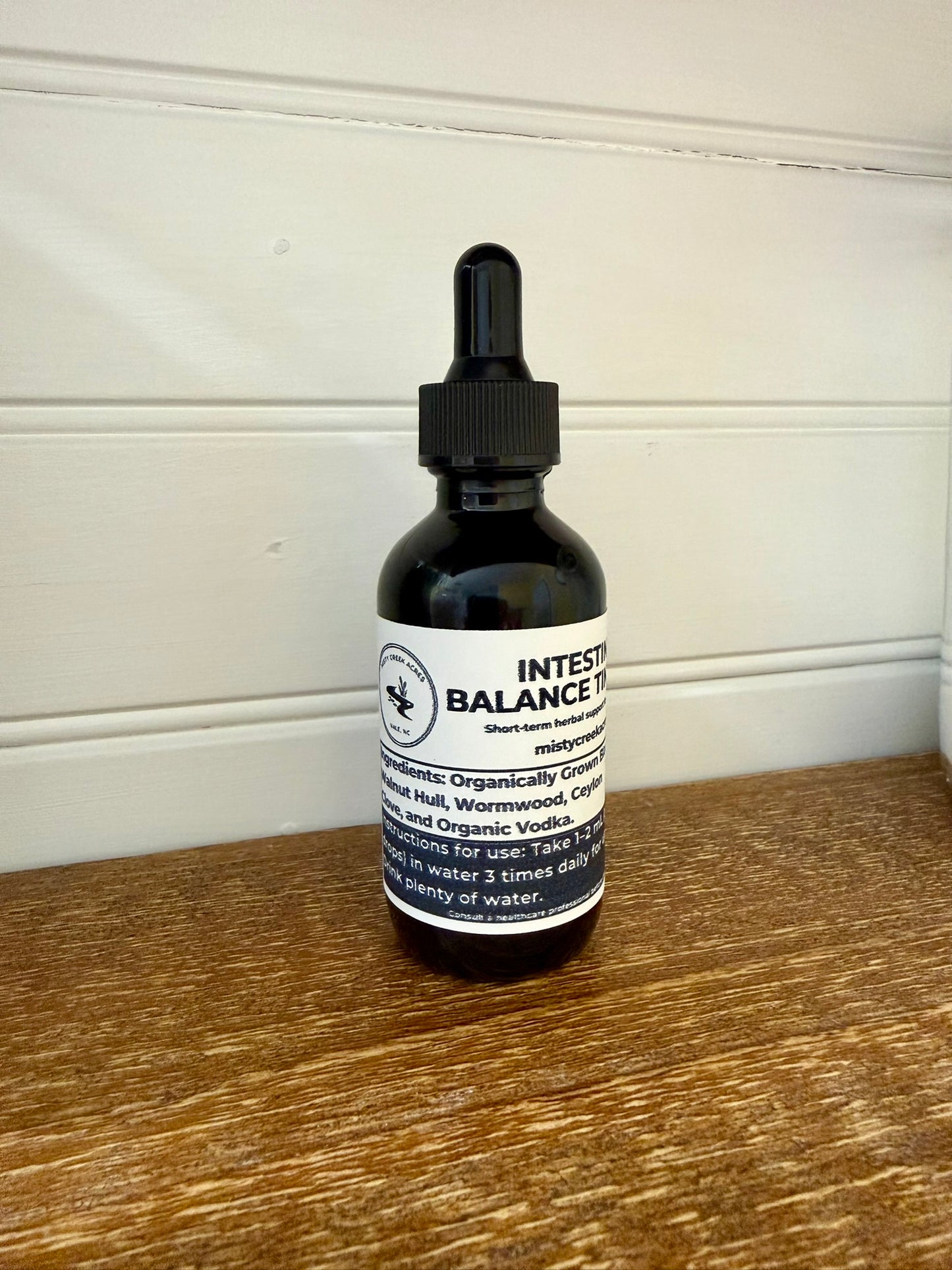 Bottle of Intestinal Balance Tonic on a wooden surface with a white wall background