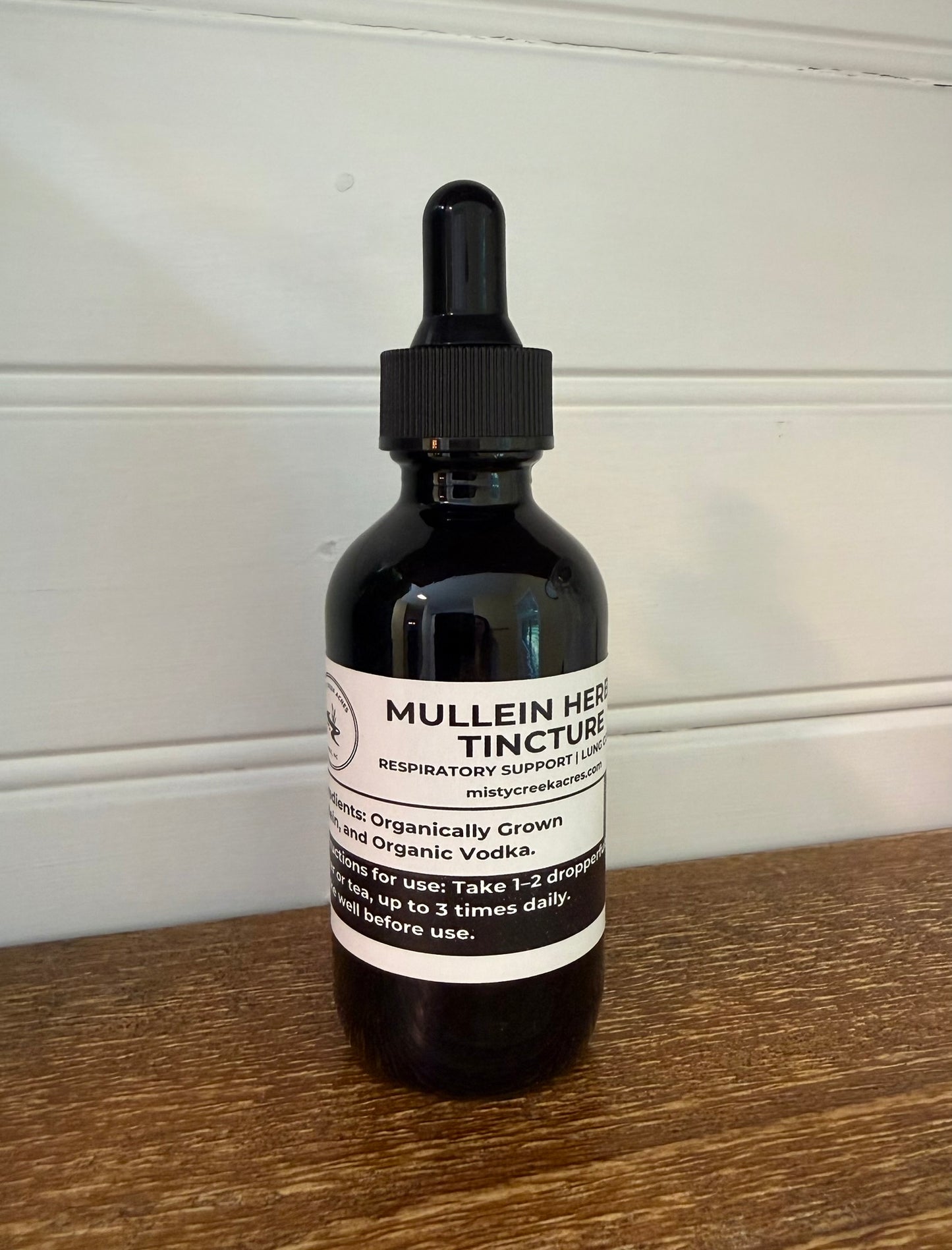 Bottle of Mullein Herb Tincture on a wooden surface with a white wall background