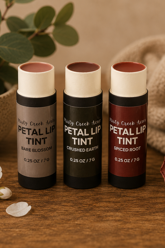 Three petal lip tint products on a wooden surface with flowers and leaves in the background.