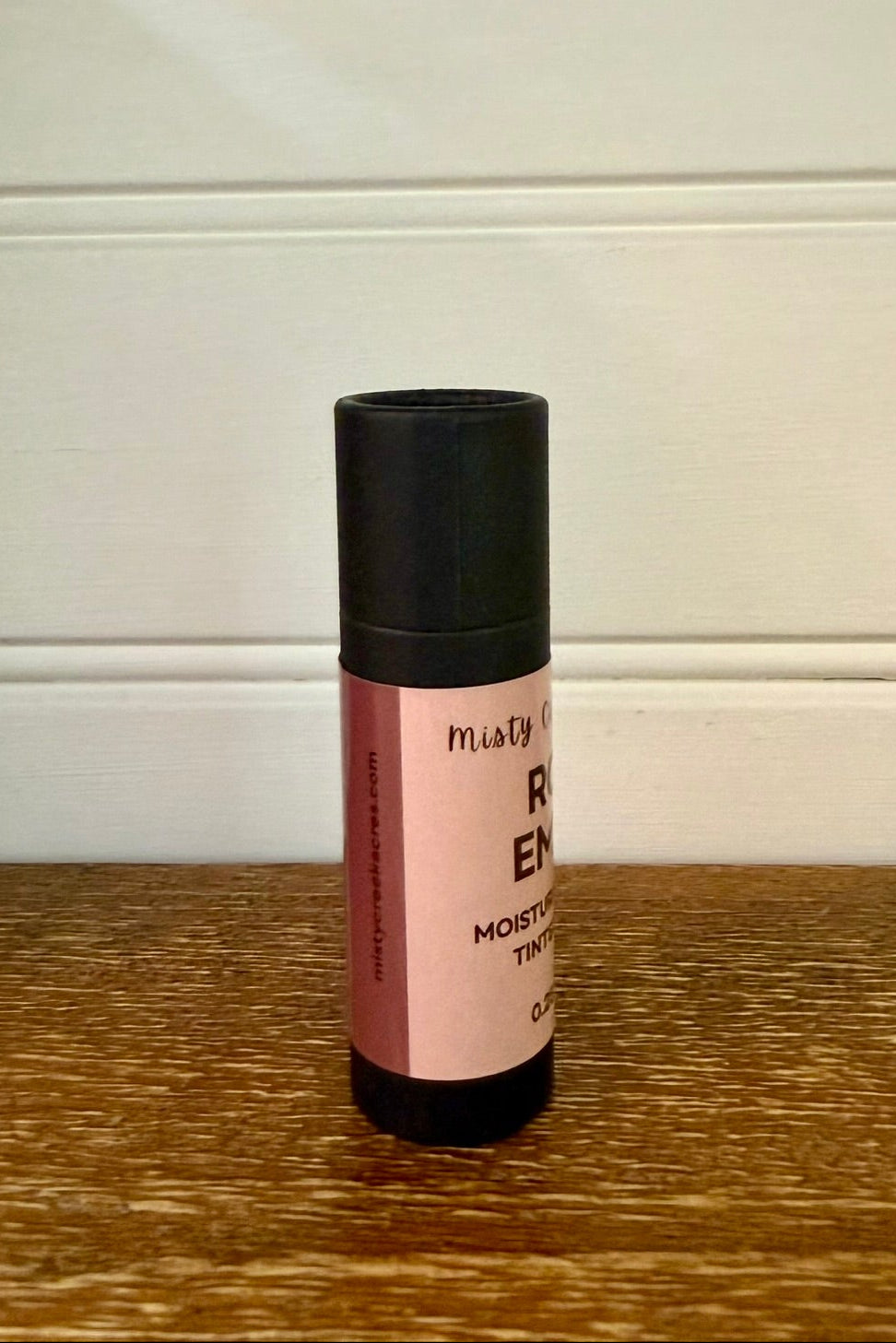 Roll-on bottle with pink label and black cap on a wooden surface.