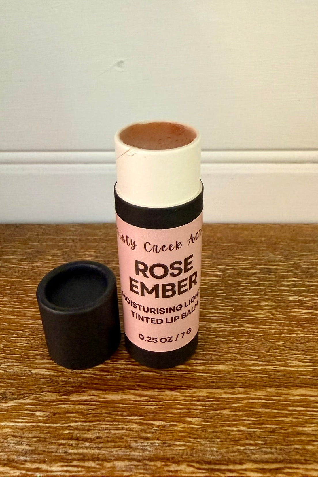 Lip balm with pink label on a wooden surface