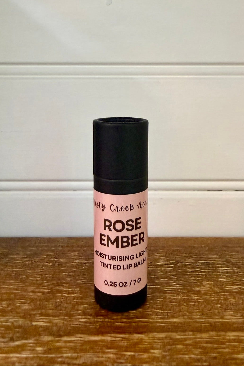 Lip balm with a black cap and pink label on a wooden surface.
