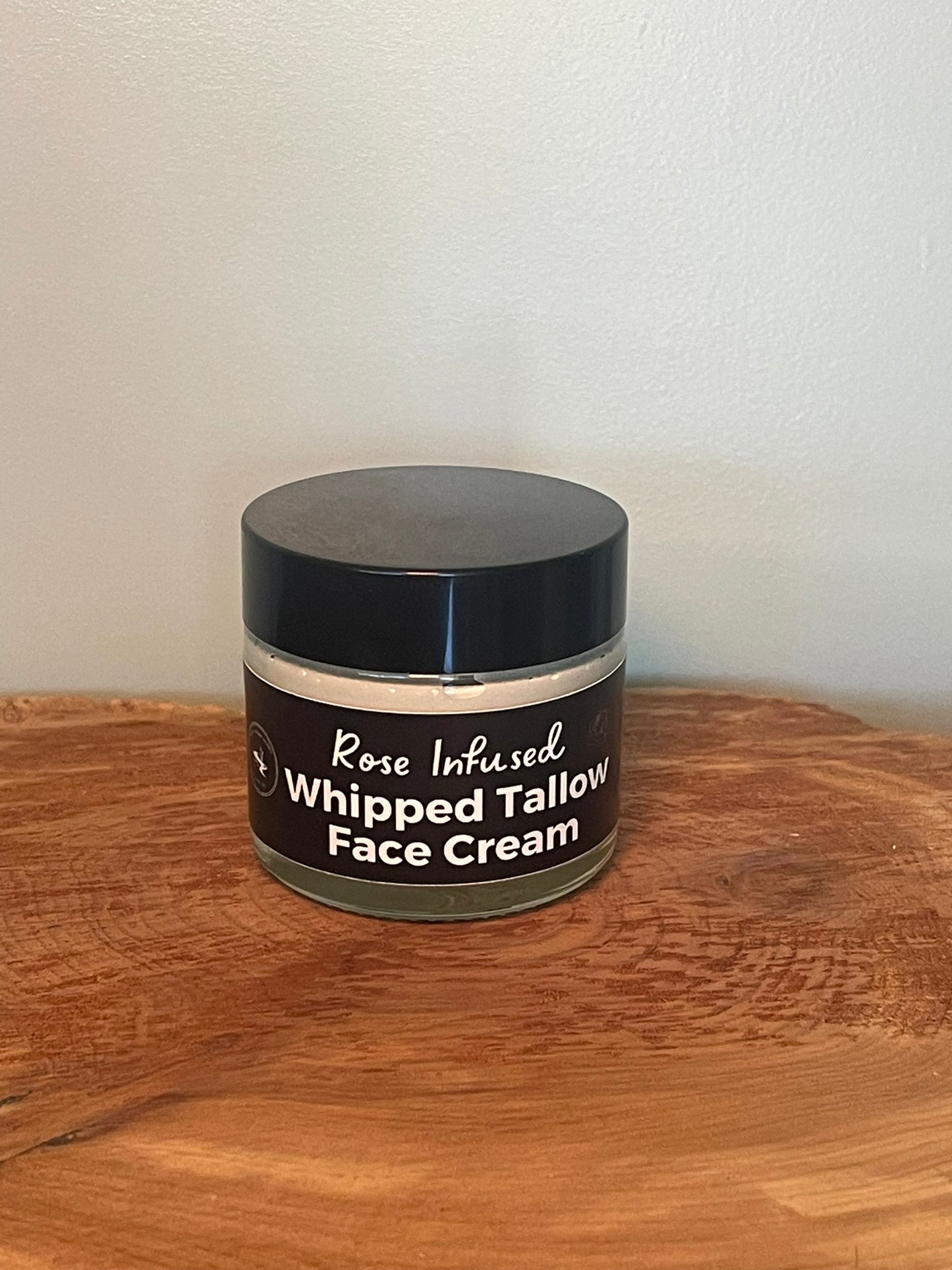 Jar of rose infused whipped tallow face cream on a wooden surface with a white background