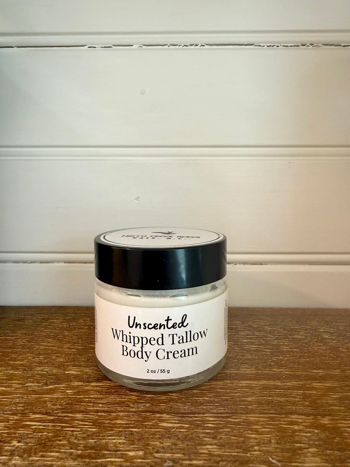 Jar of unscented whipped tallow body cream on a wooden surface with a white background
