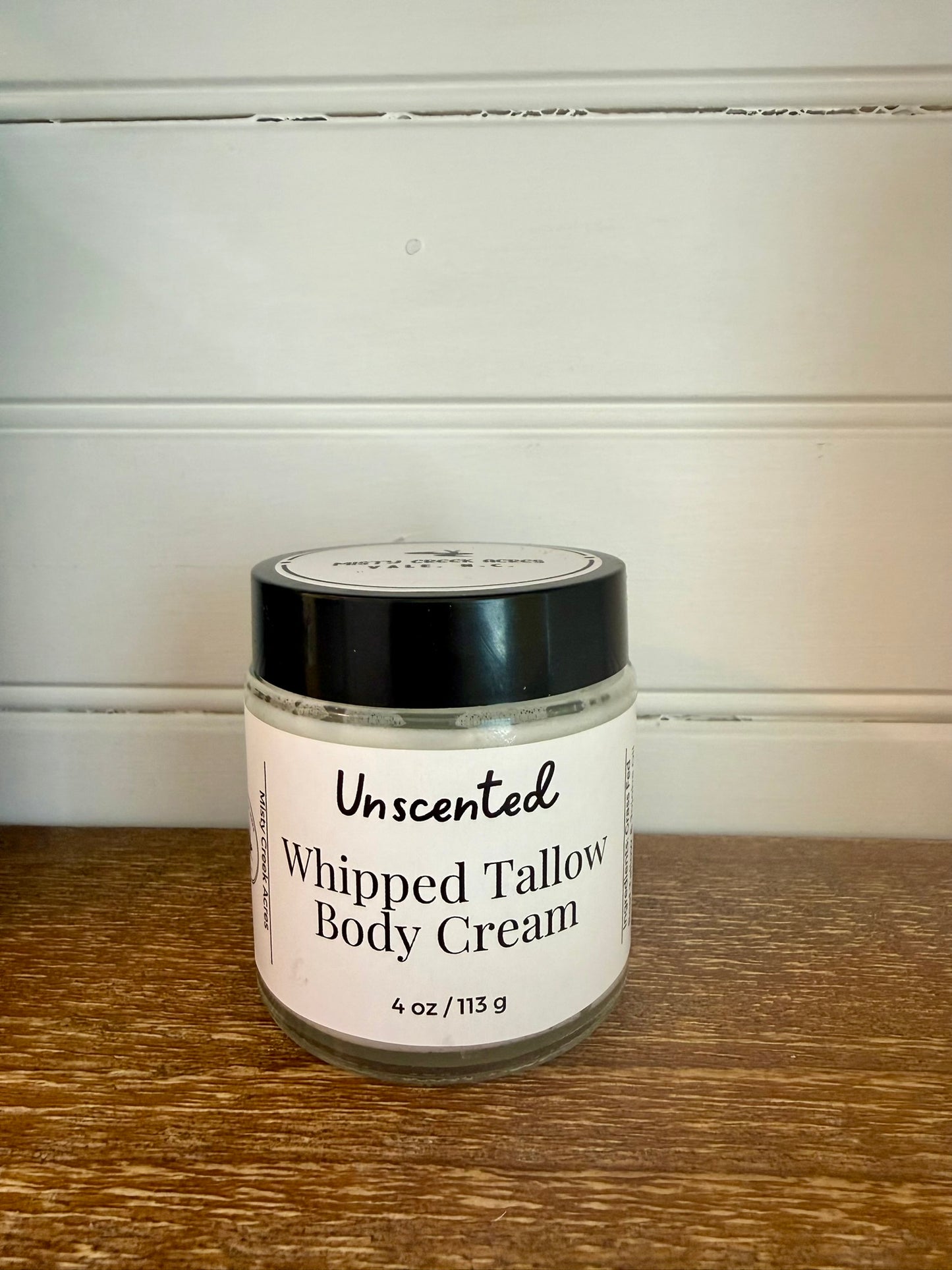 Jar of unscented whipped tallow body cream on a wooden surface with a white wall background