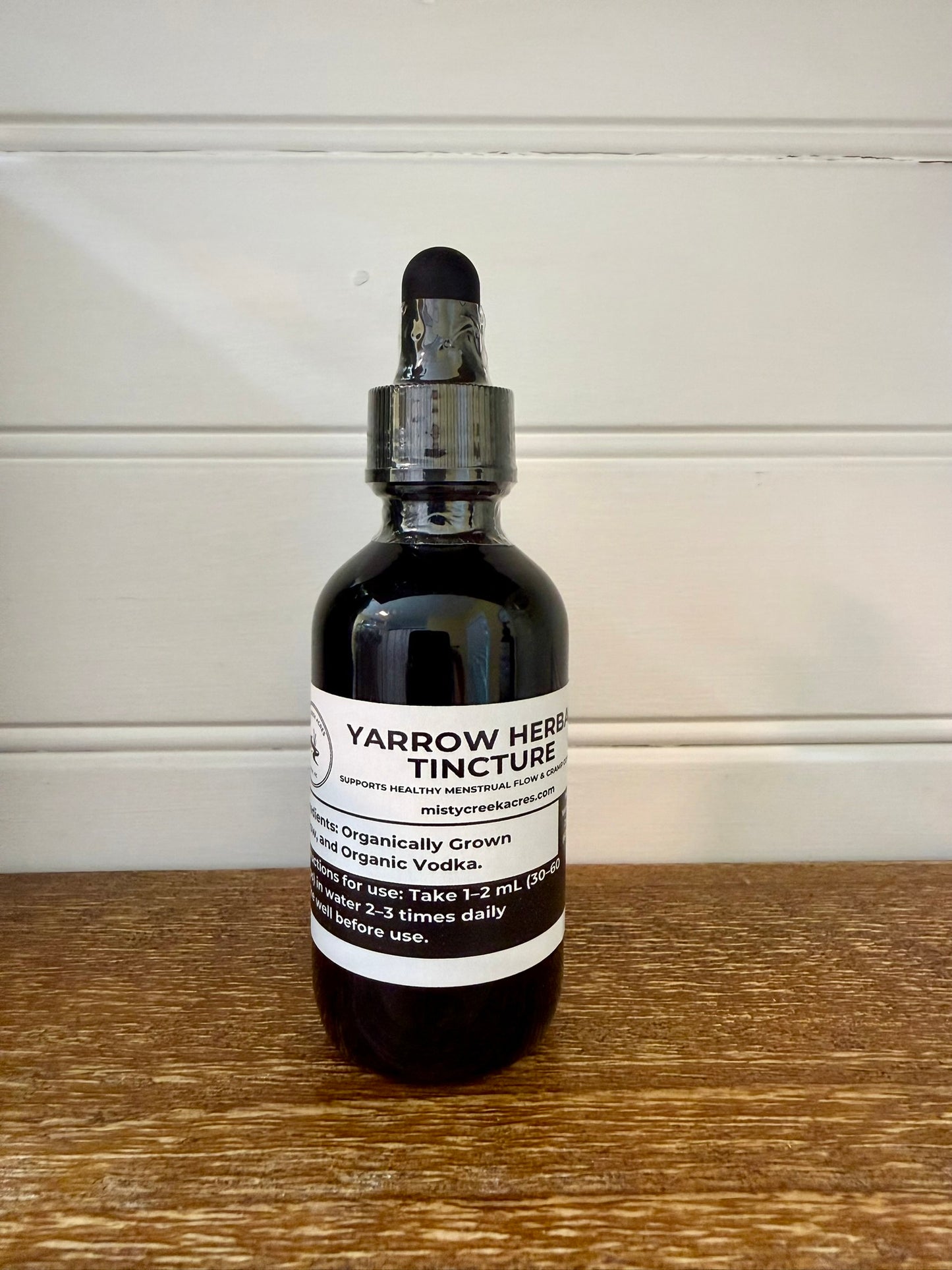 Bottle of Yarrow Herb Tincture on a wooden surface with a white wall background