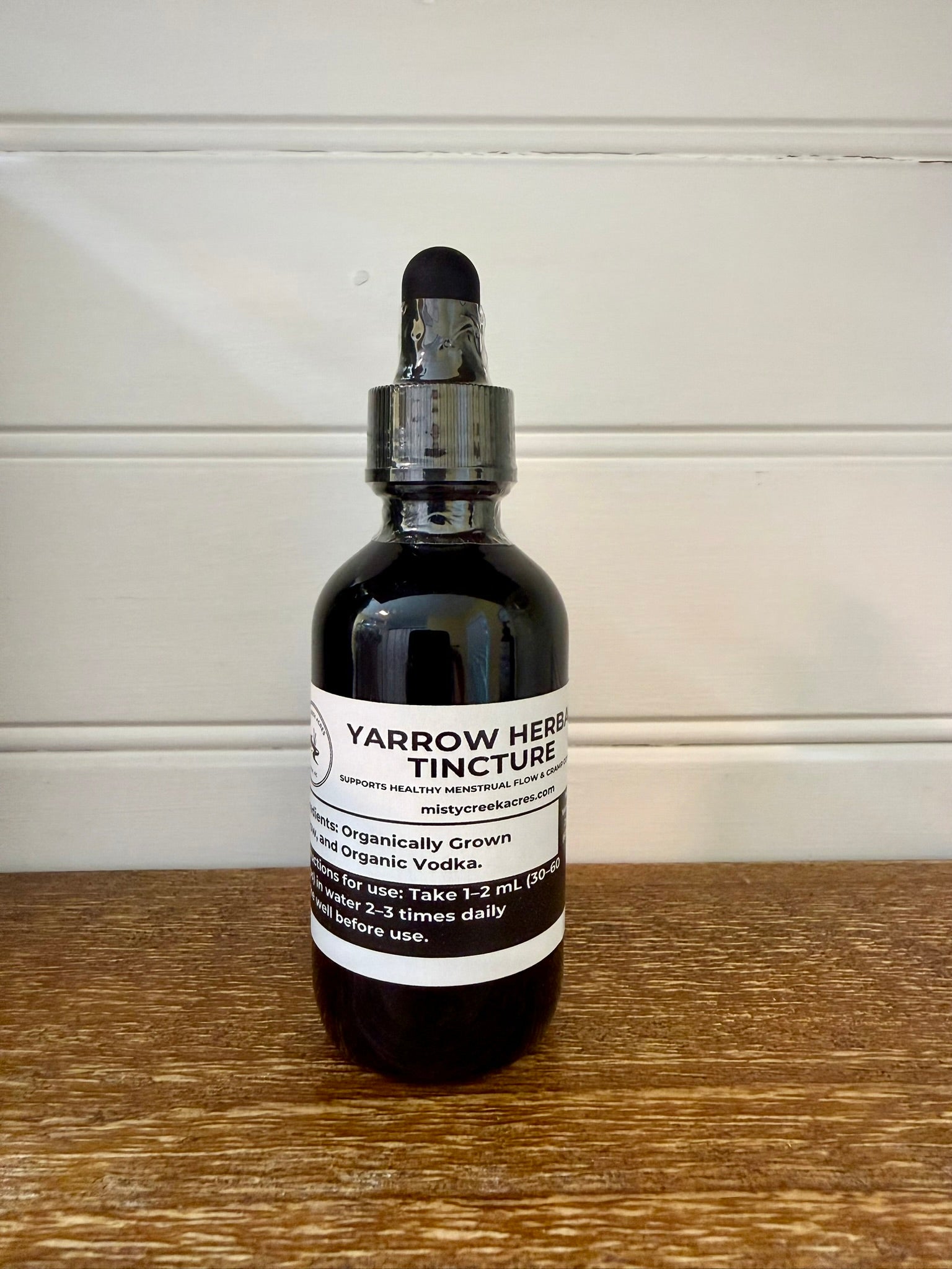 Bottle of Yarrow Herb Tincture on a wooden surface with a white wall background