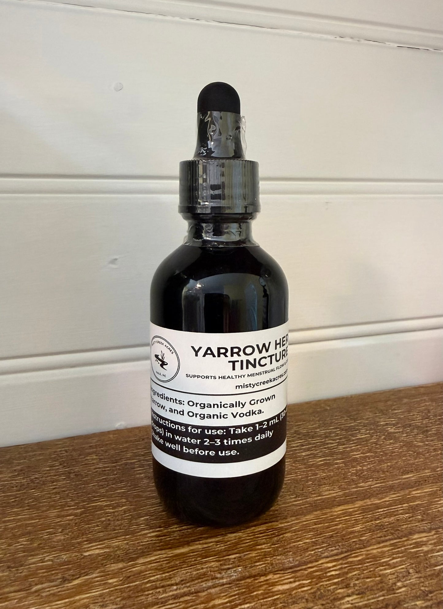 Bottle of Yarrow Herb Tincture on a wooden surface with a white wall background