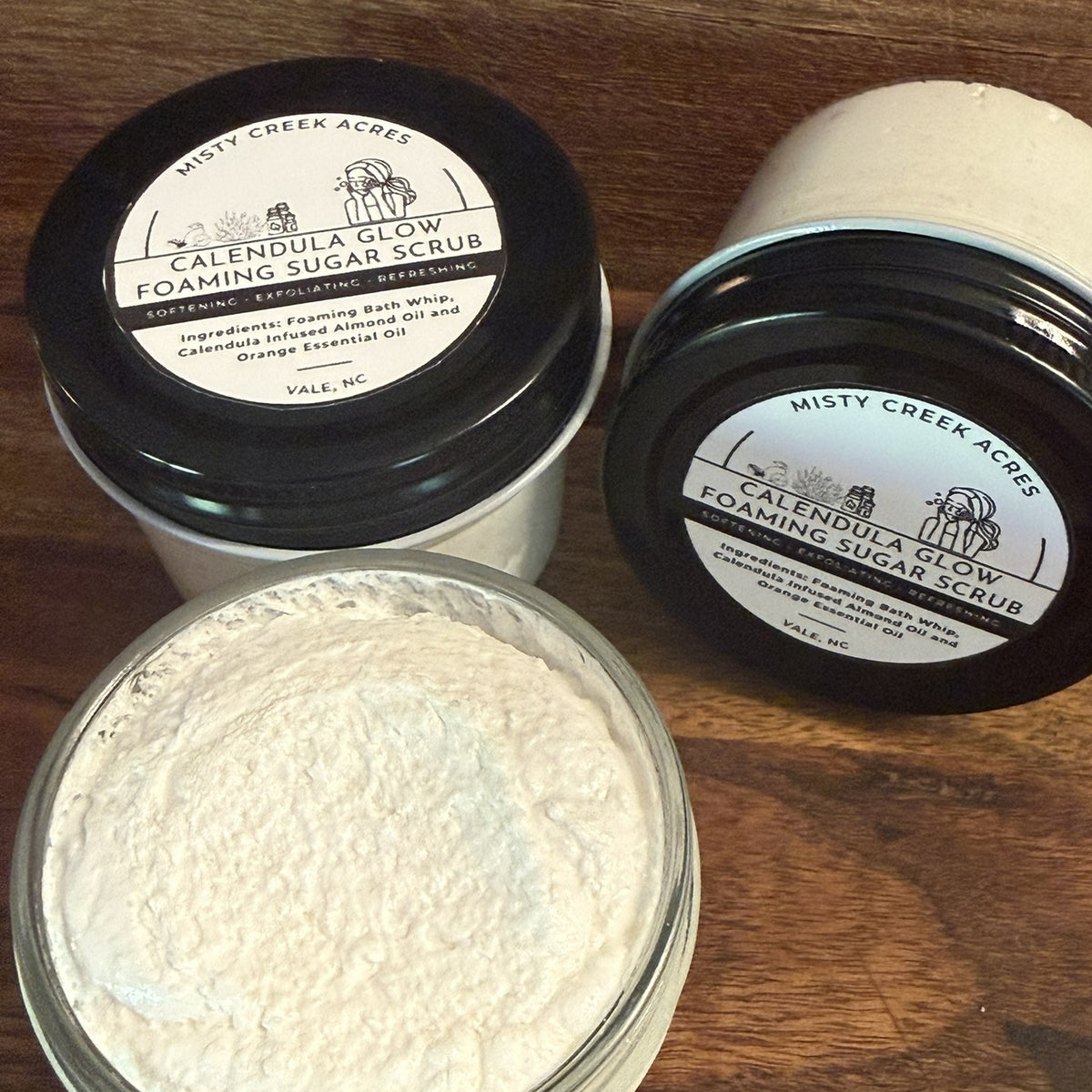 Open jar of Calendula Glow Foaming Sugar Scrub on rustic wood – Misty Creek Acres