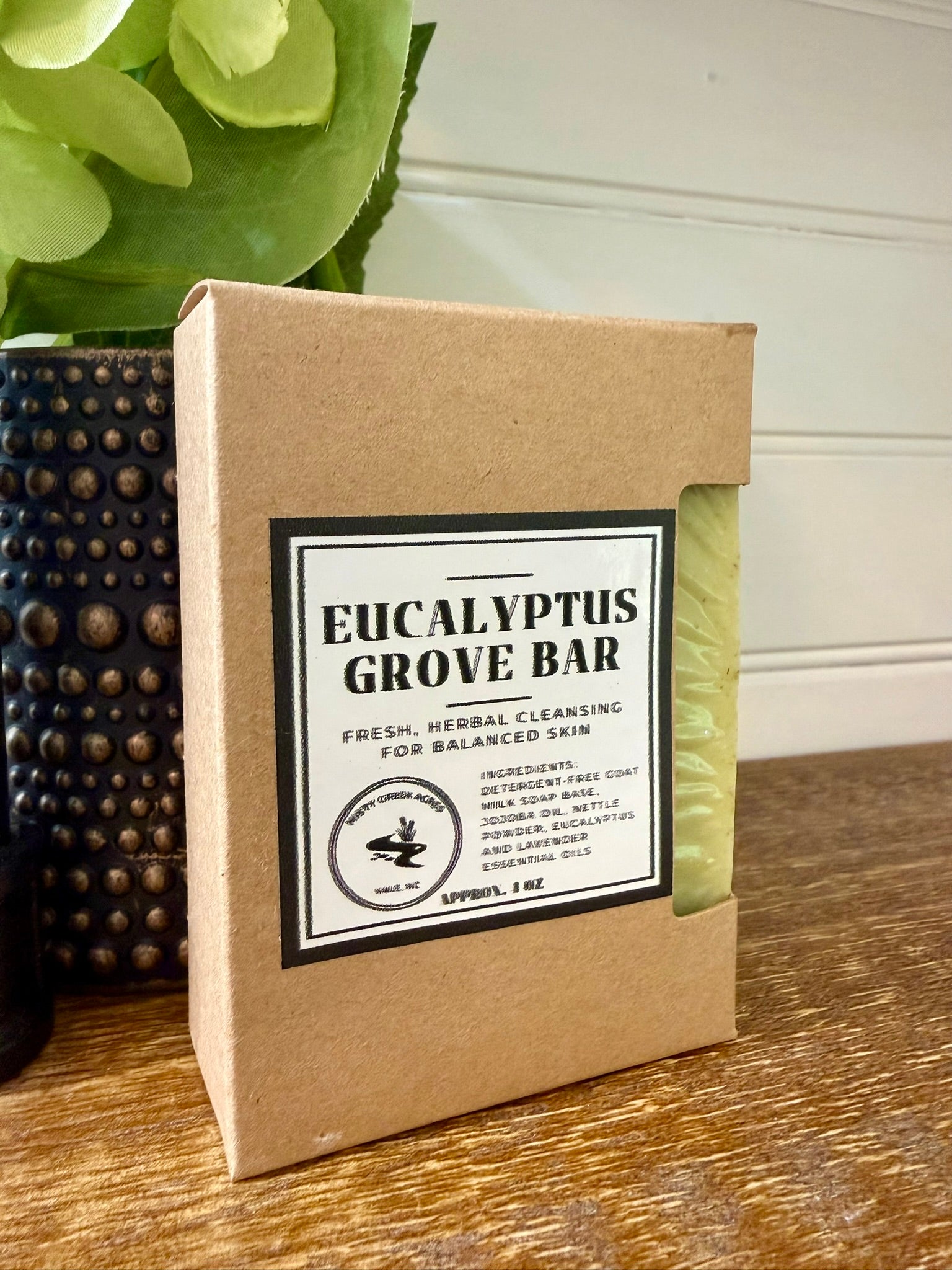 Eucalyptus Grove Bar soap in a brown cardboard box on a wooden surface with a plant in the background.