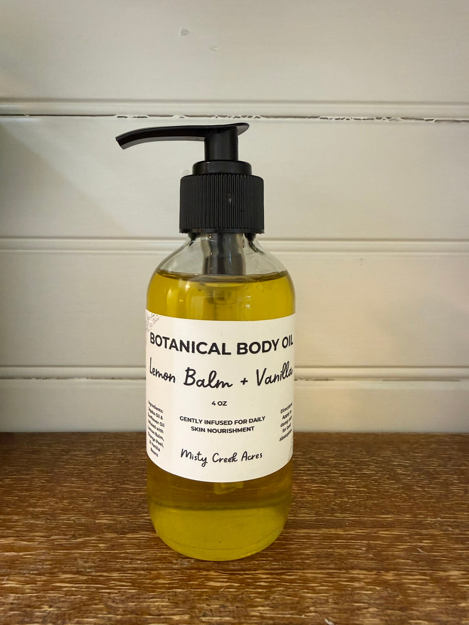 Bottle of botanical body oil with a pump on a wooden surface and white wall background