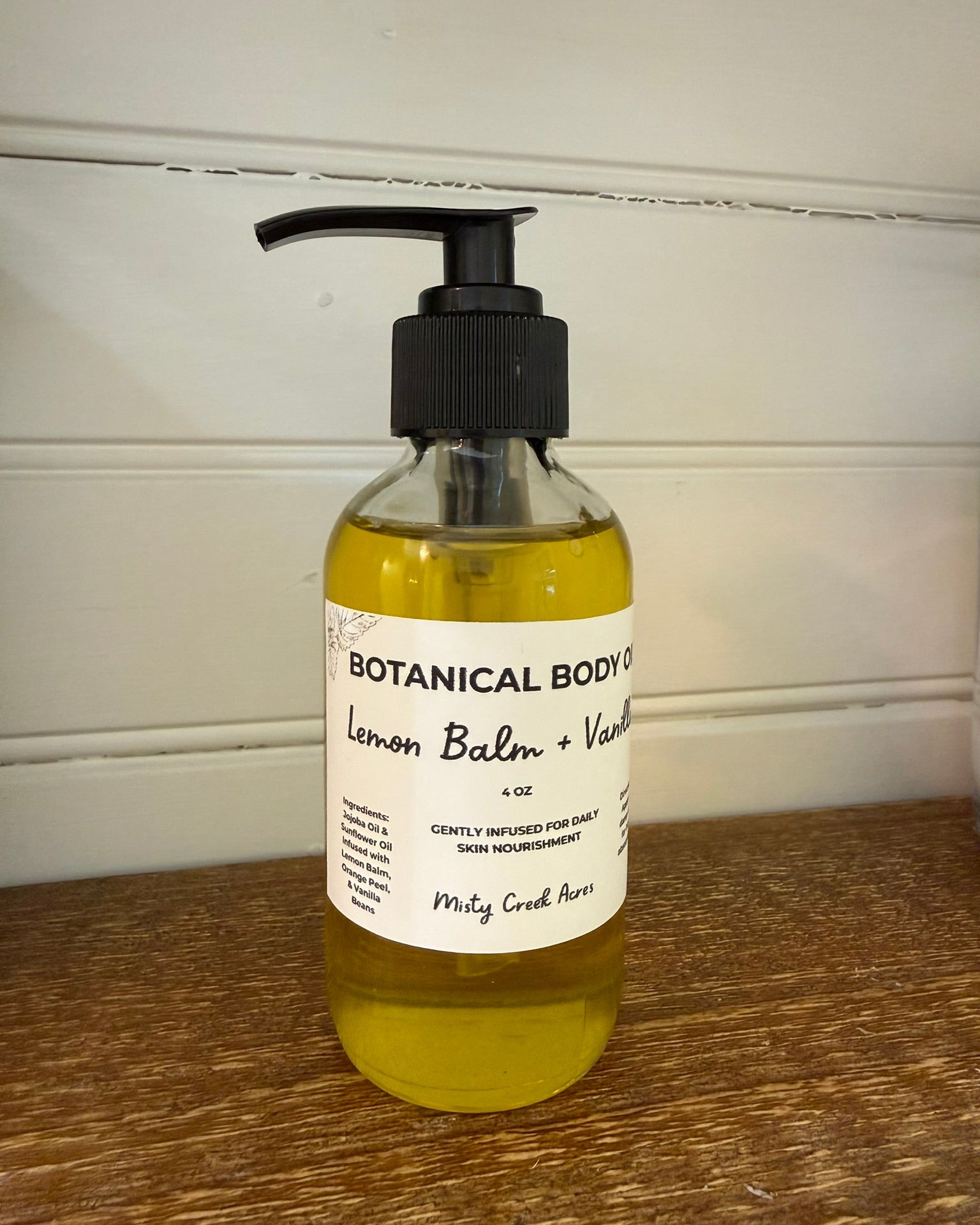 Bottle of Botanical Body Co. Lemon Balm & Vanilla soap on a wooden surface with a white wall background.