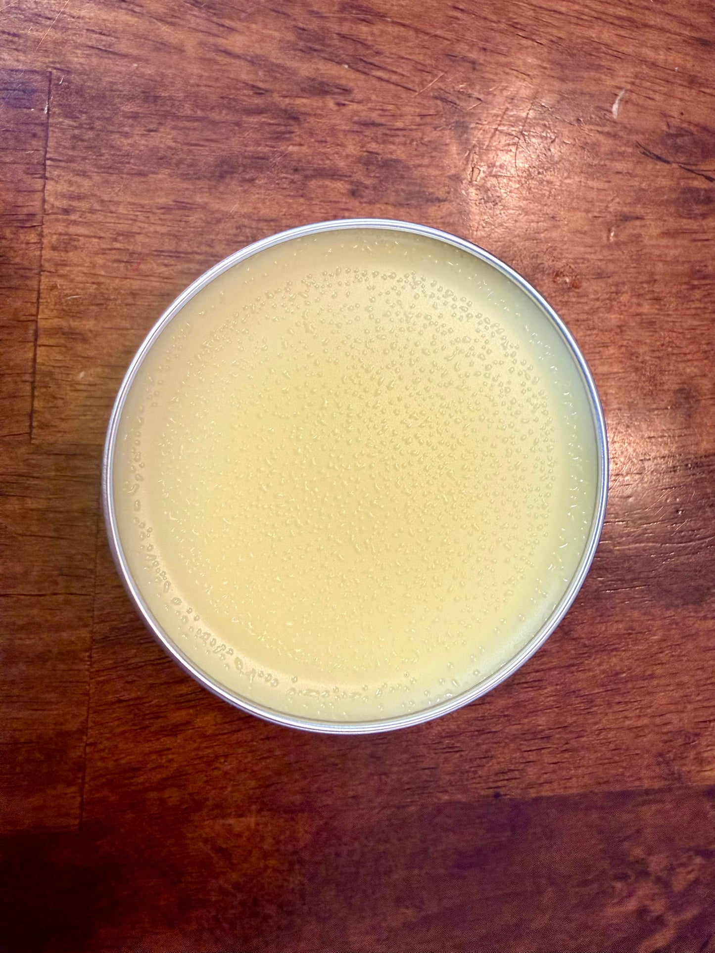 Round salve in a pink tin on a wooden surface