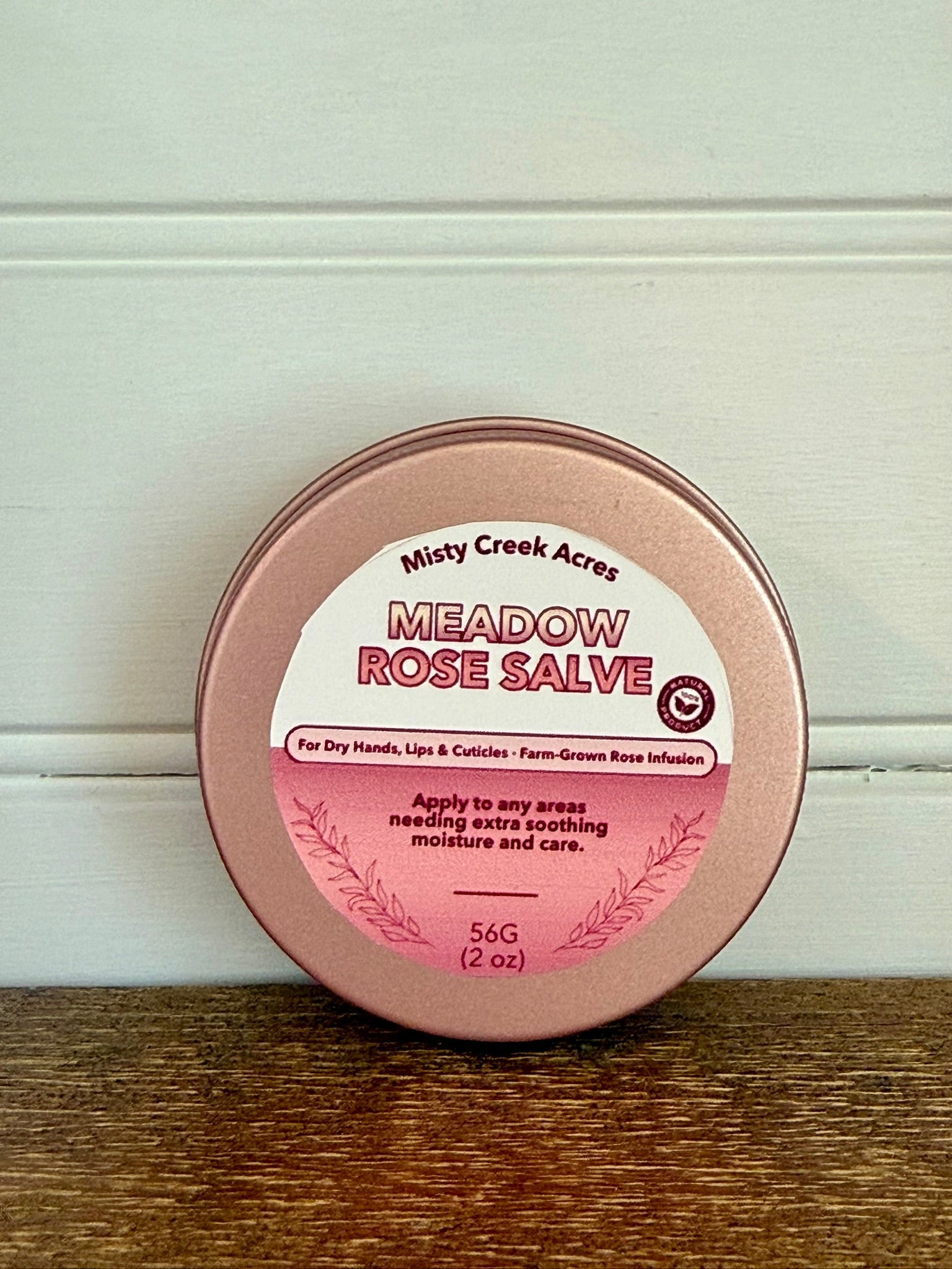 Meadow Rose Salve container with pink lid and white label on a wooden surface.