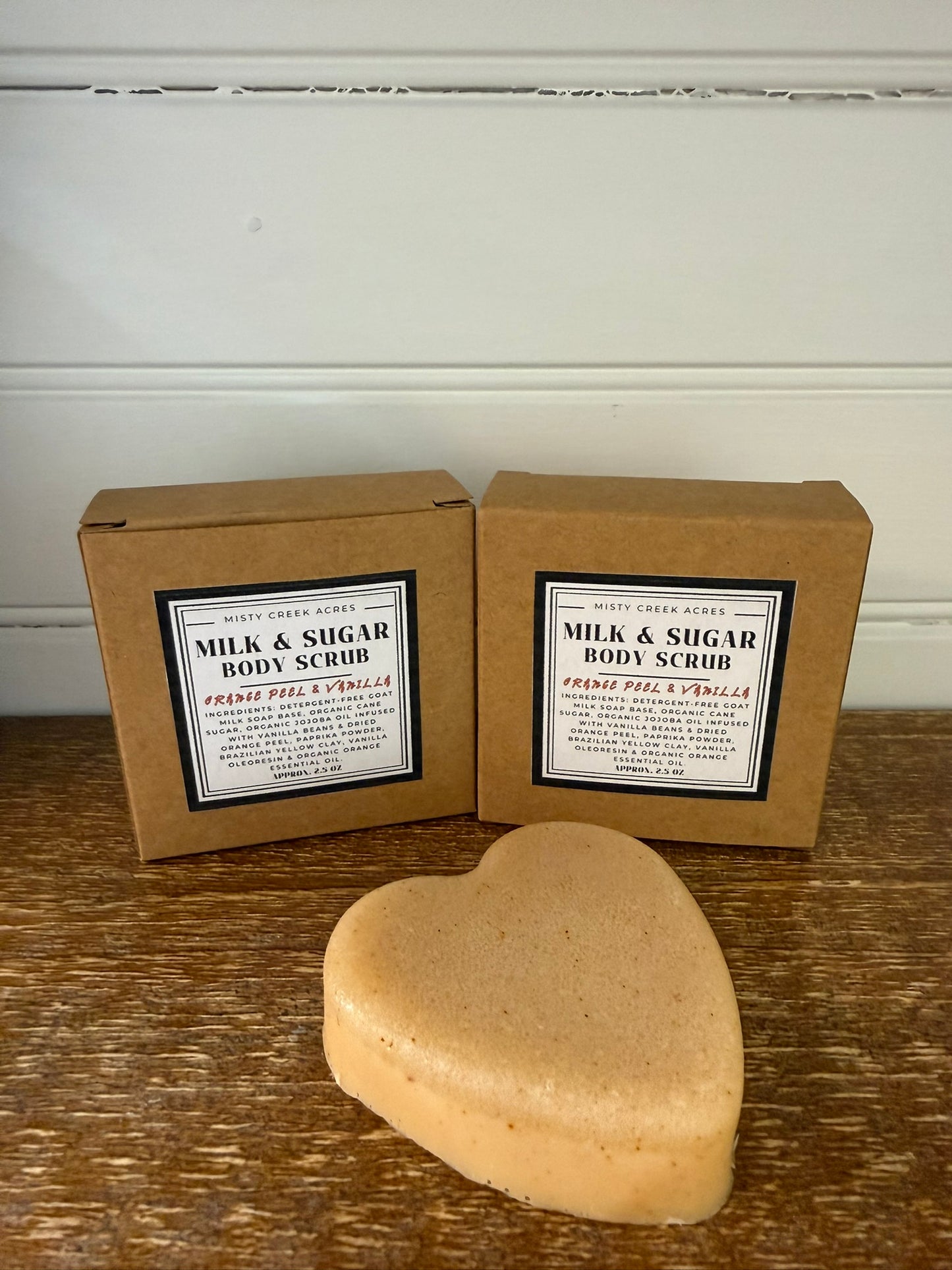 Heart-shaped body scrub with two boxes labeled 'Milk & Sugar Body Scrub' on a wooden surface.