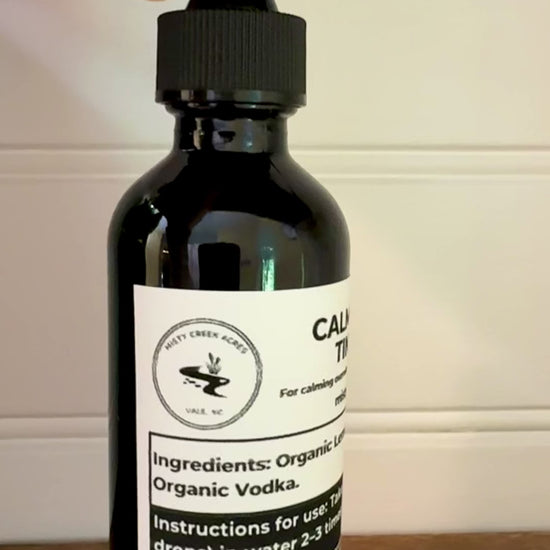 Bottle of Calm Clarity Tincture on a wooden surface with a white wall background