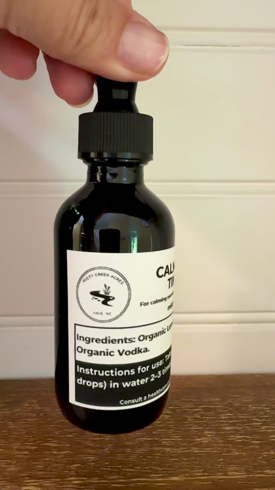 Bottle of Calm Clarity Tincture on a wooden surface with a white wall background