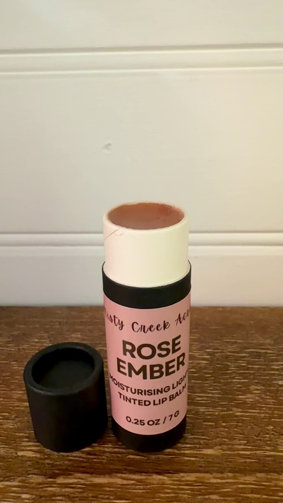 Lip balm with pink label on a wooden surface