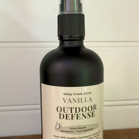 Bottle of Vanilla Outdoor Defense spray on a wooden surface with a white background