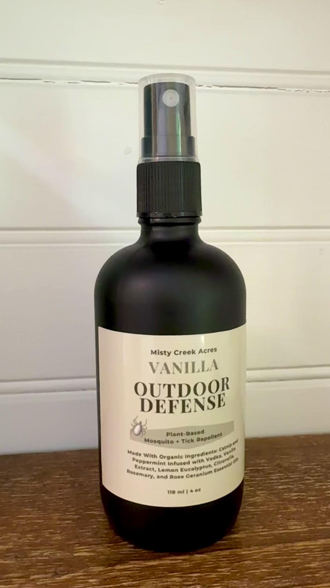 Bottle of Vanilla Outdoor Defense spray on a wooden surface with a white background