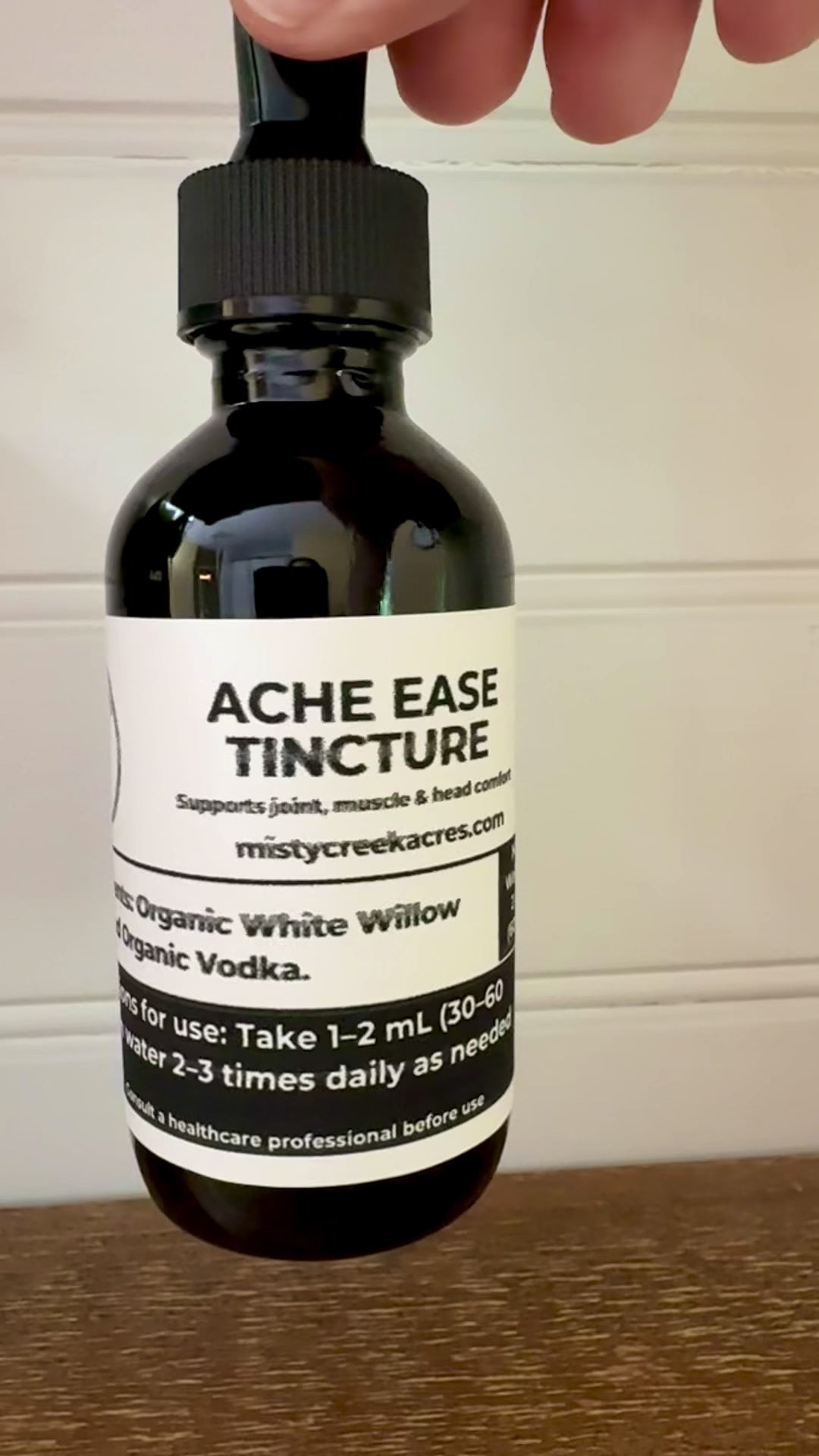 Bottle of Acme Ease Tincture on a wooden surface with a white wall background