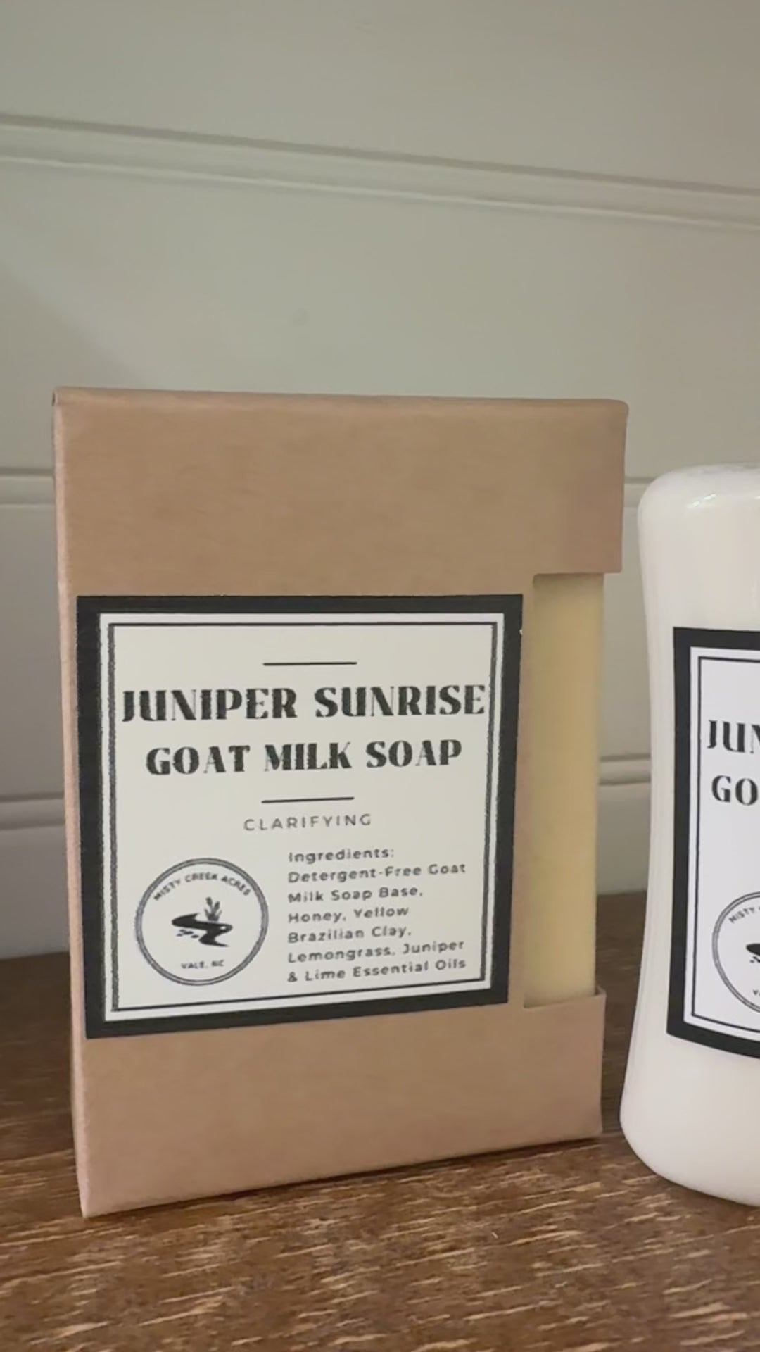 Juniper Sunrise Goat Milk Soap and Goat Milk Lotion set, featuring a kraft paper box of soap and a white bottle of lotion on a wooden surface with a green plant in the background.